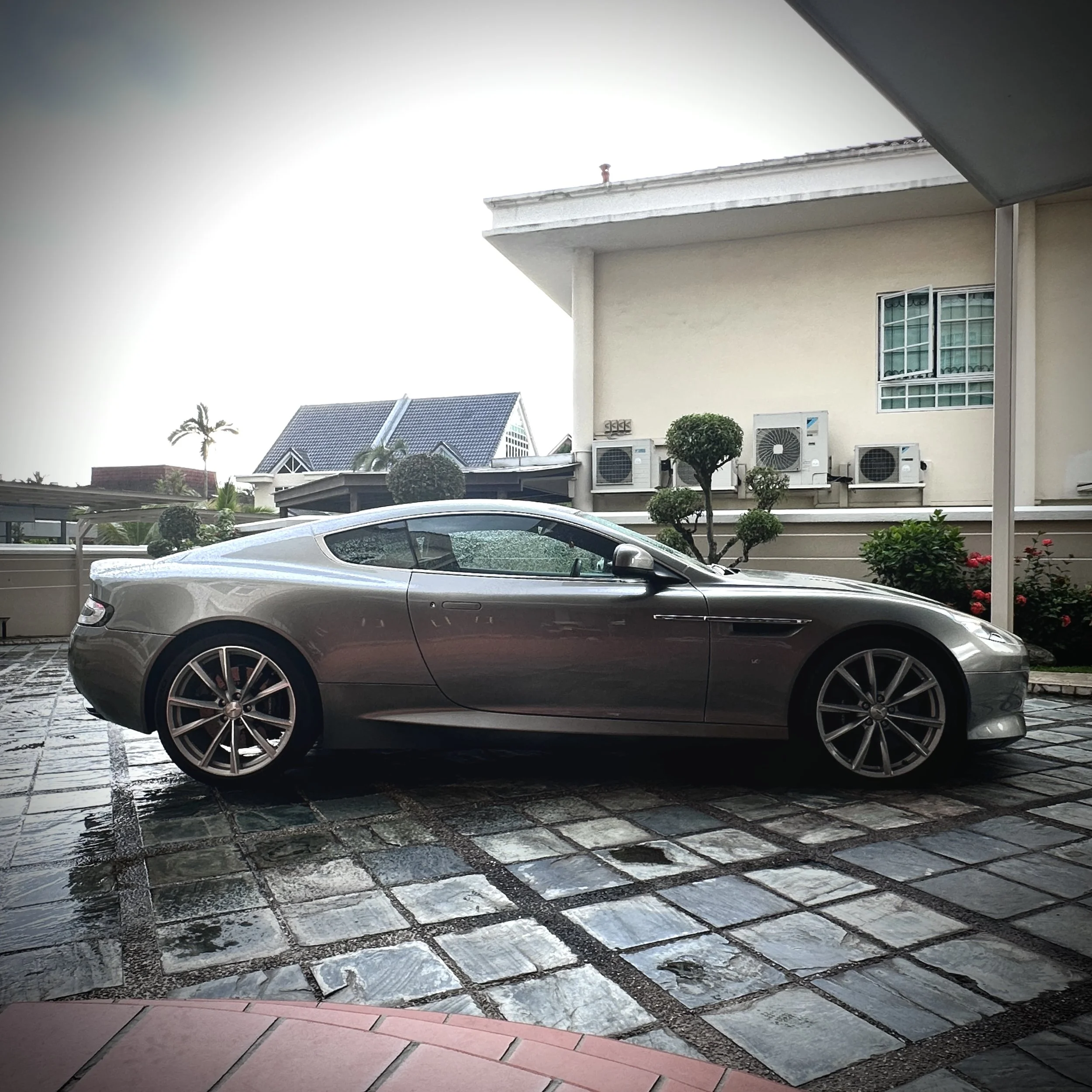 Silver sports car parked on driveway outside modern house with tiled roof and square windows.