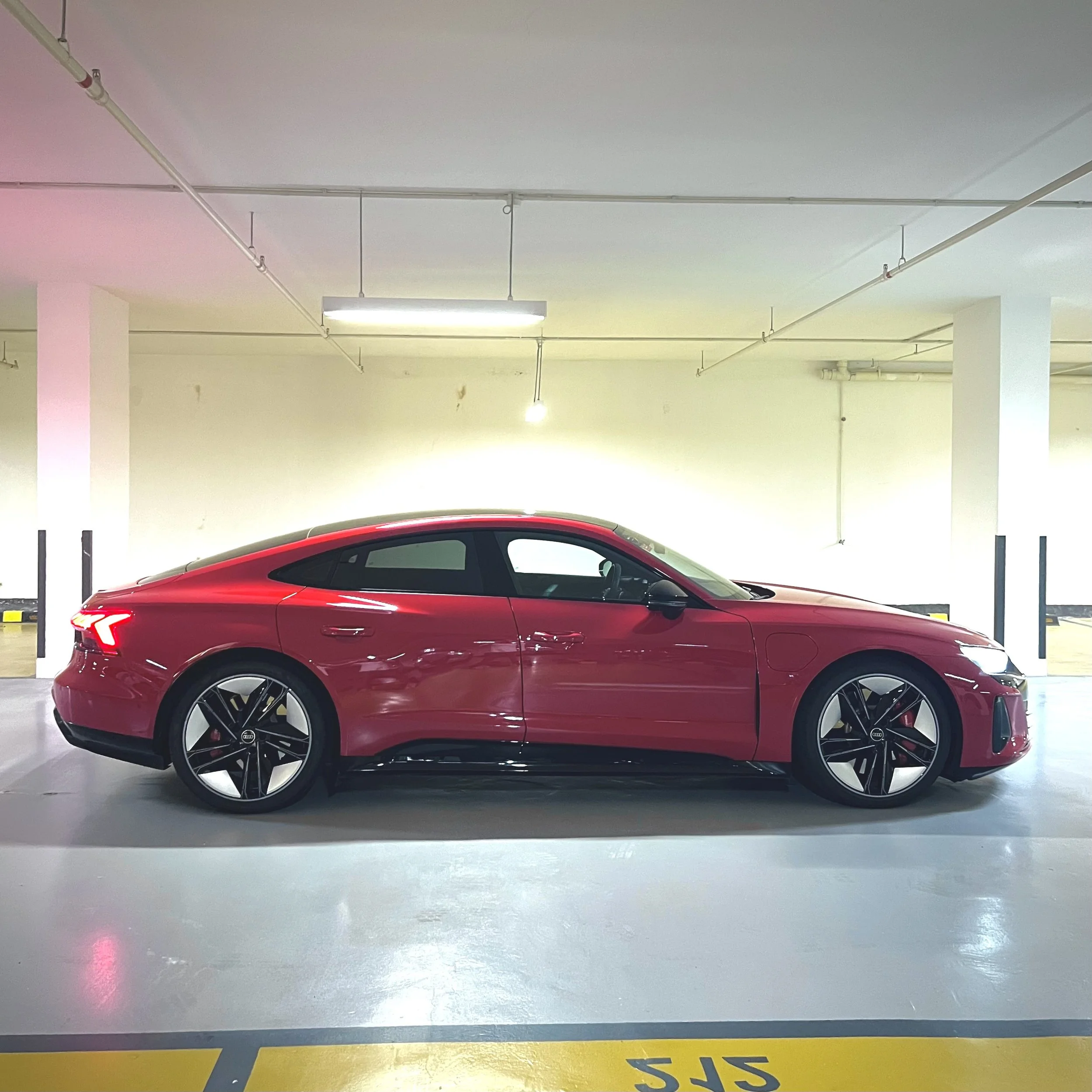 Red luxury sports car parked in a garage with clean white walls and overhead lighting.