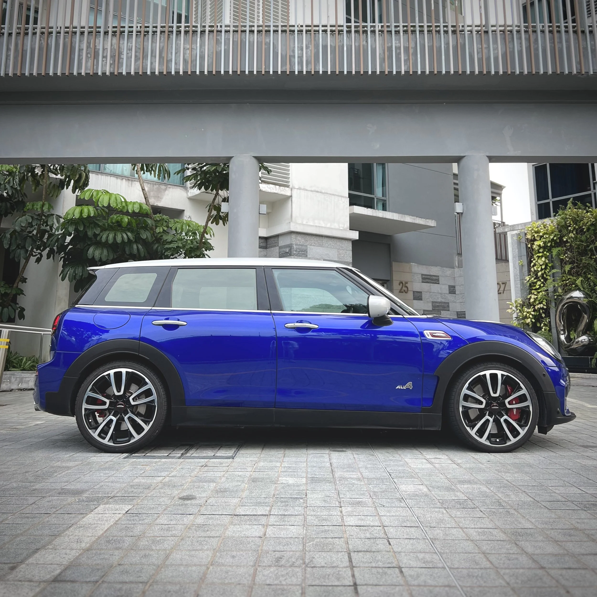 Blue Mini Clubman parked in front of a modern building with greenery.