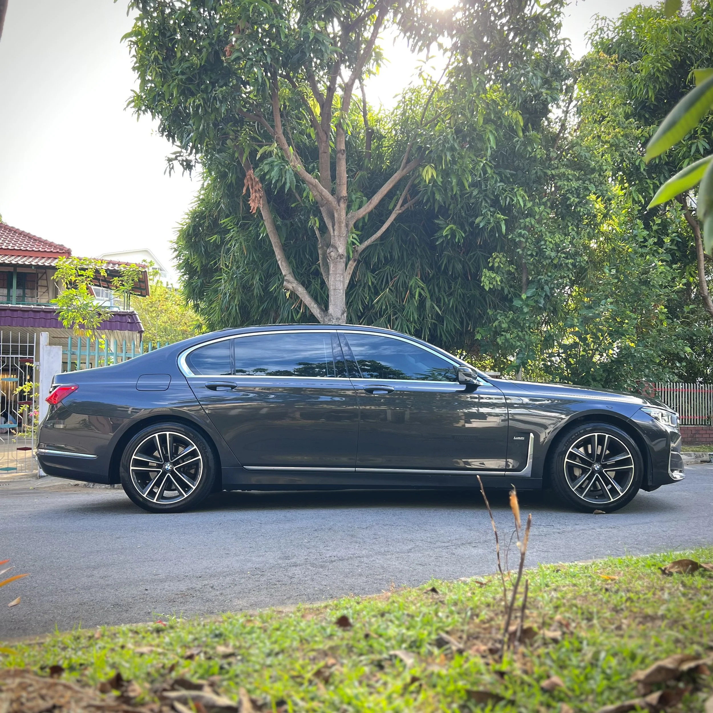 Gray luxury sedan parked on a street near trees and a residential house.