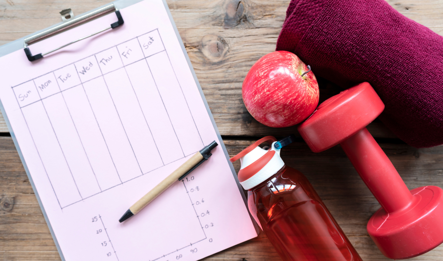 Weekly training schedule planner with dumbbells and water bottle showing consistent workout frequency planning for sustainable fitness