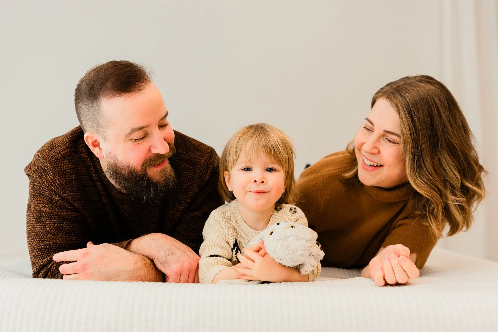 Perhekuvaus studiolla Tampereella, koko perhe makoilee vatsallaan sängyllä.