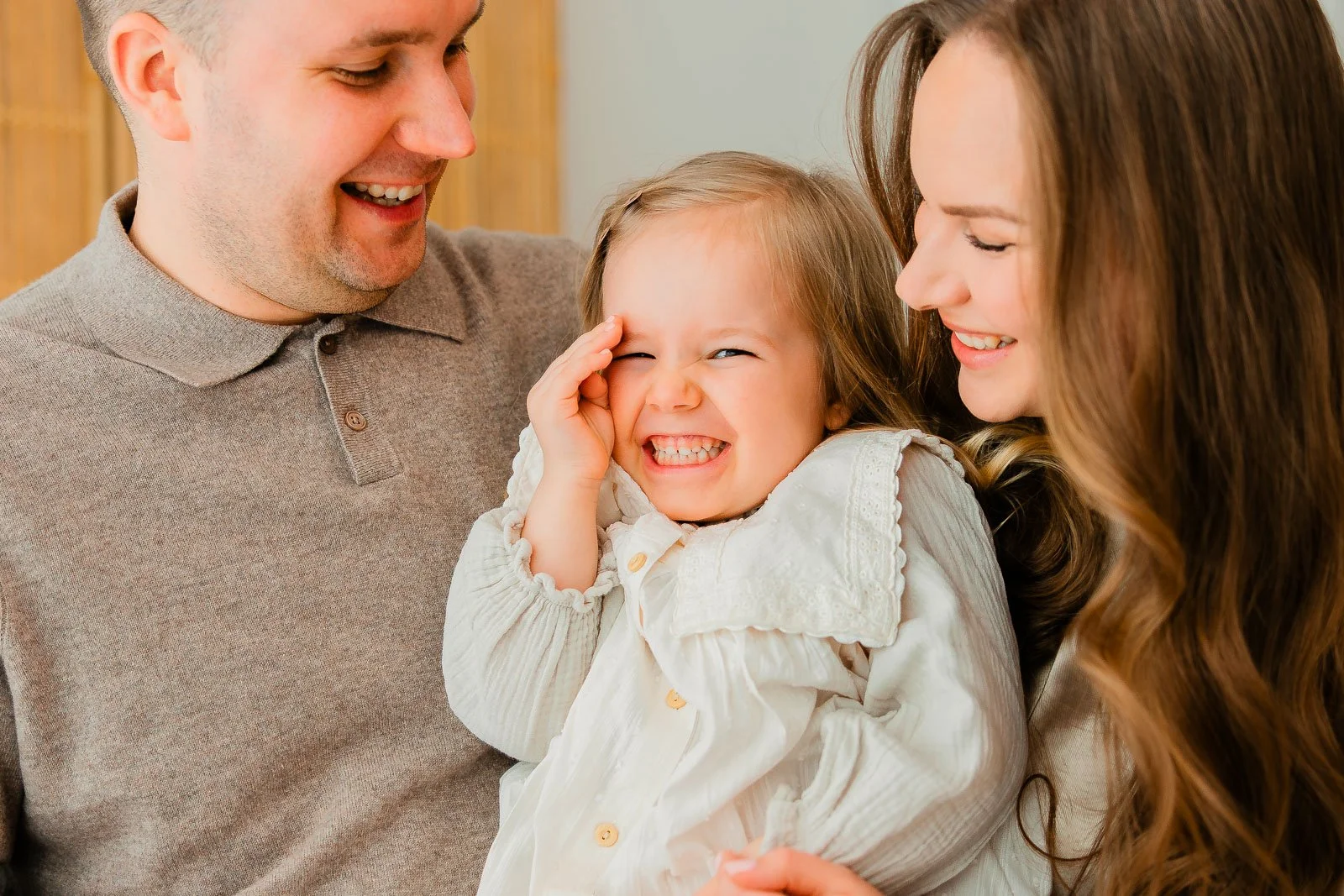 Tampereen studiolla kuvattu perhekuva, lapsi nauraa keskellä ja vanhemmat katsovat häntä sivusta.