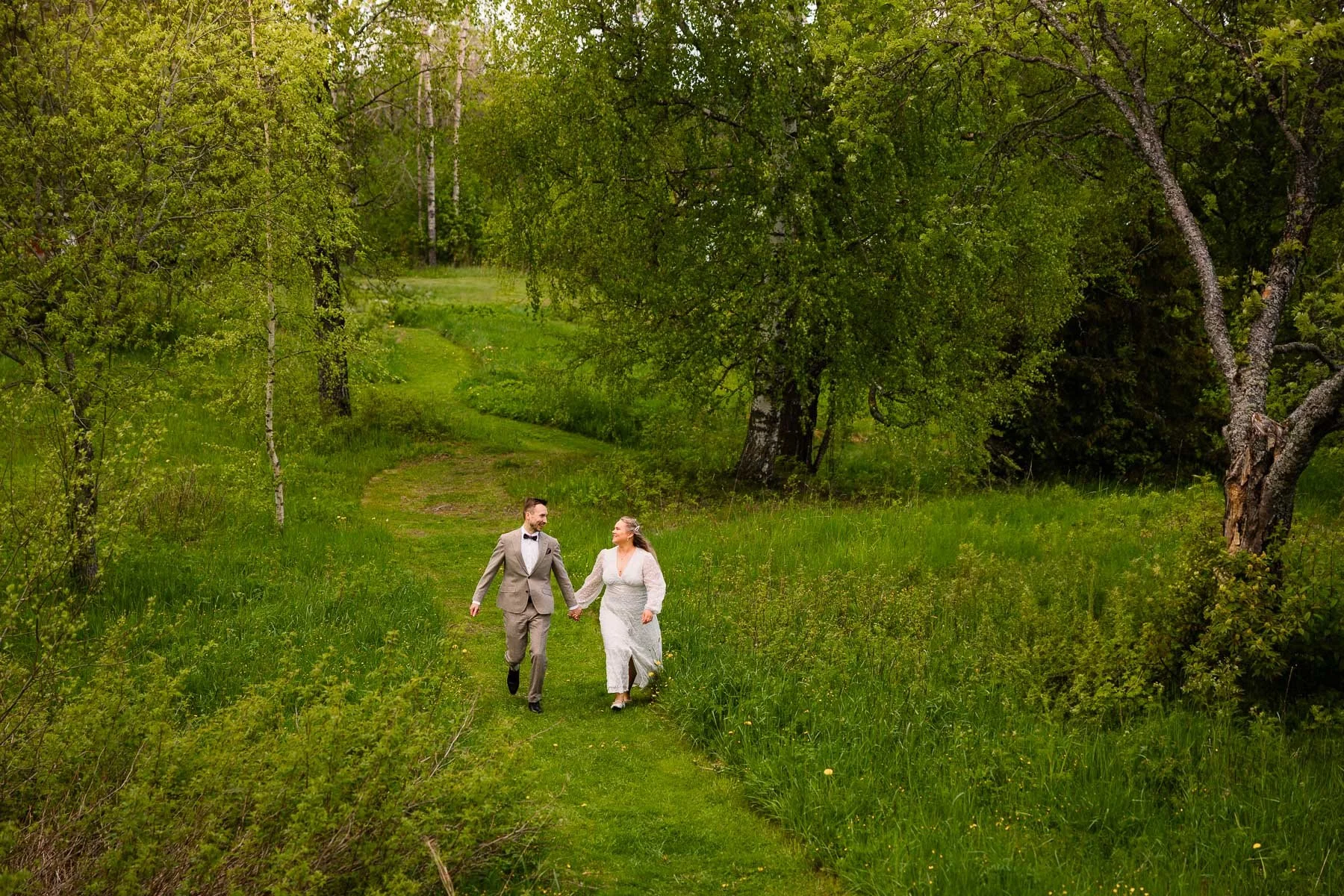 Hääkuva, jossa hääpari juoksee kohti kameraa vihreän niityn keskellä.