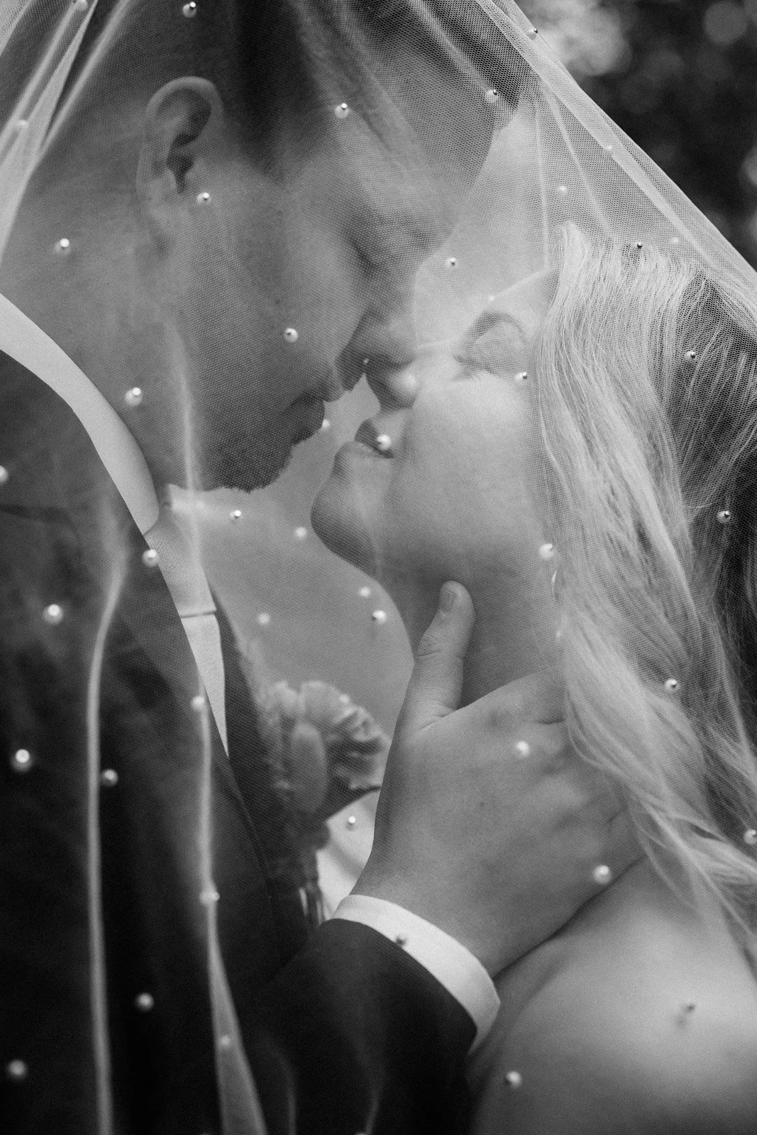 Mustavalkoinen hääkuva hääparista hunnun alla.