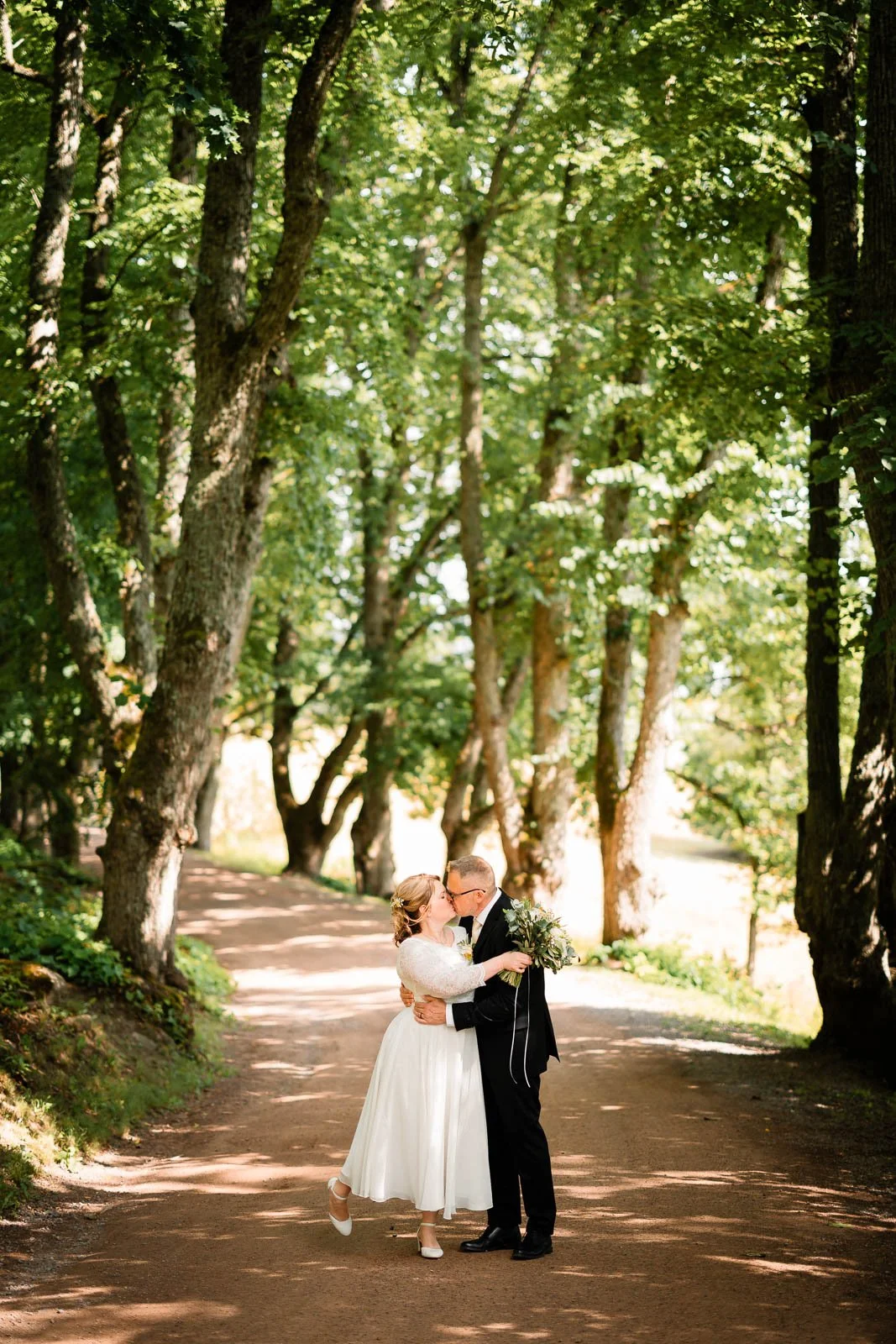 Hääkuva, jossa hääpari suutelee vihreän kujan keskellä.