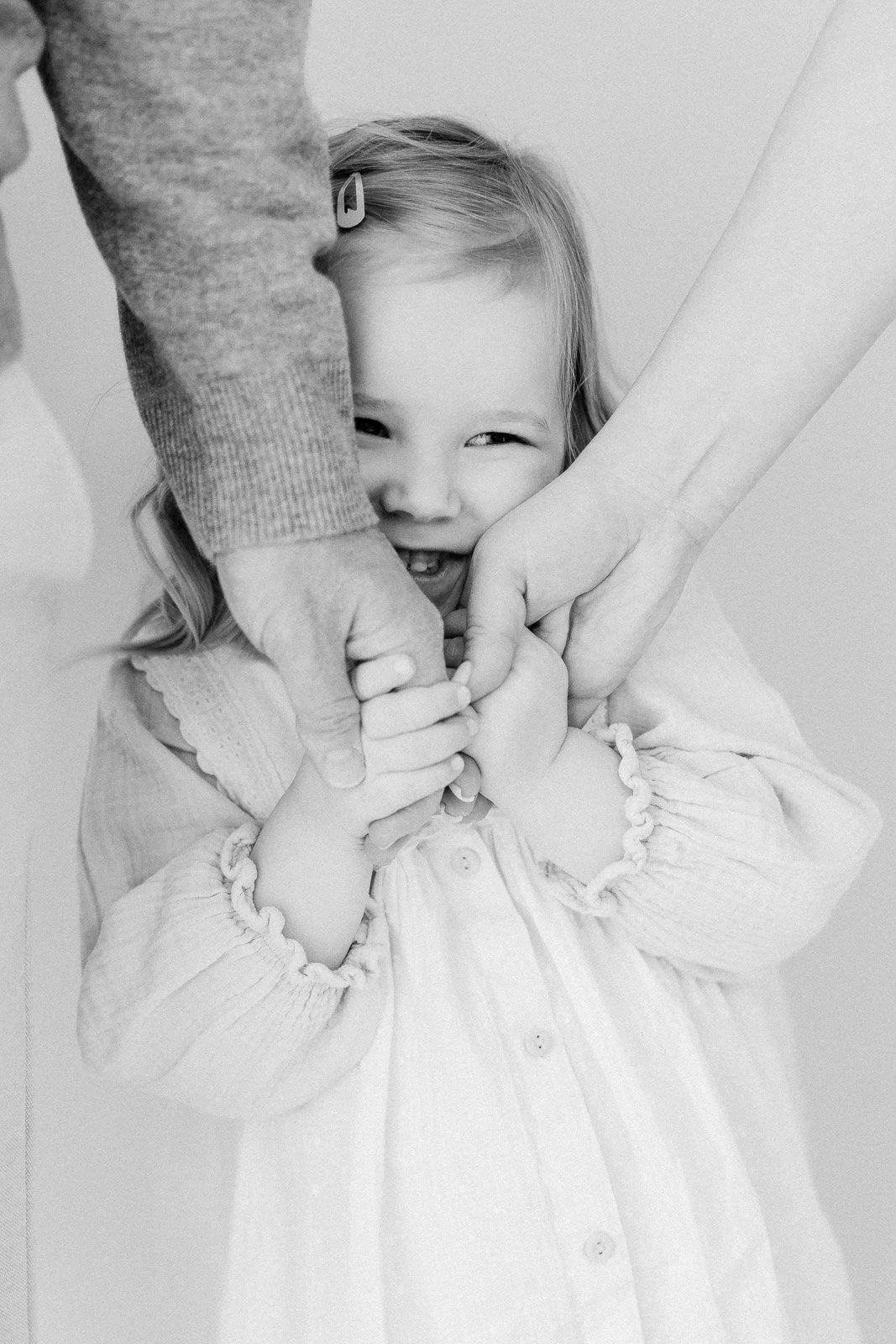 Mustavalkoinen lapsikuva studiolla Tampereella, lapsi halaa isän ja äidin kättä.