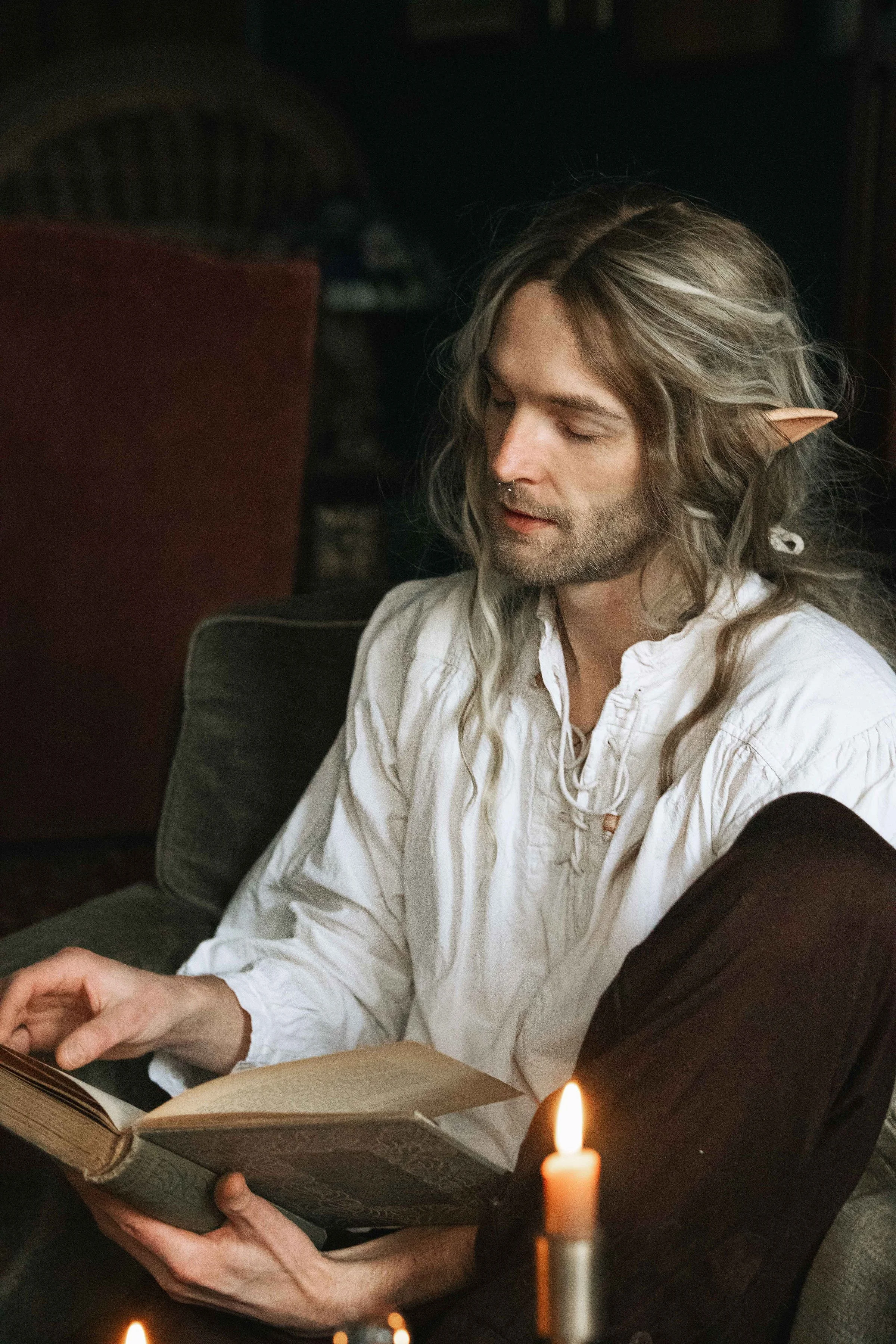 Dreamy fine art portrait of Rico as a scholar reading by candlelight. Painterly fantasy photography inspired by folklore and classical paintings, featuring books, glass bottles and warm light. Moody, romantic storytelling imagery in a fine art studio