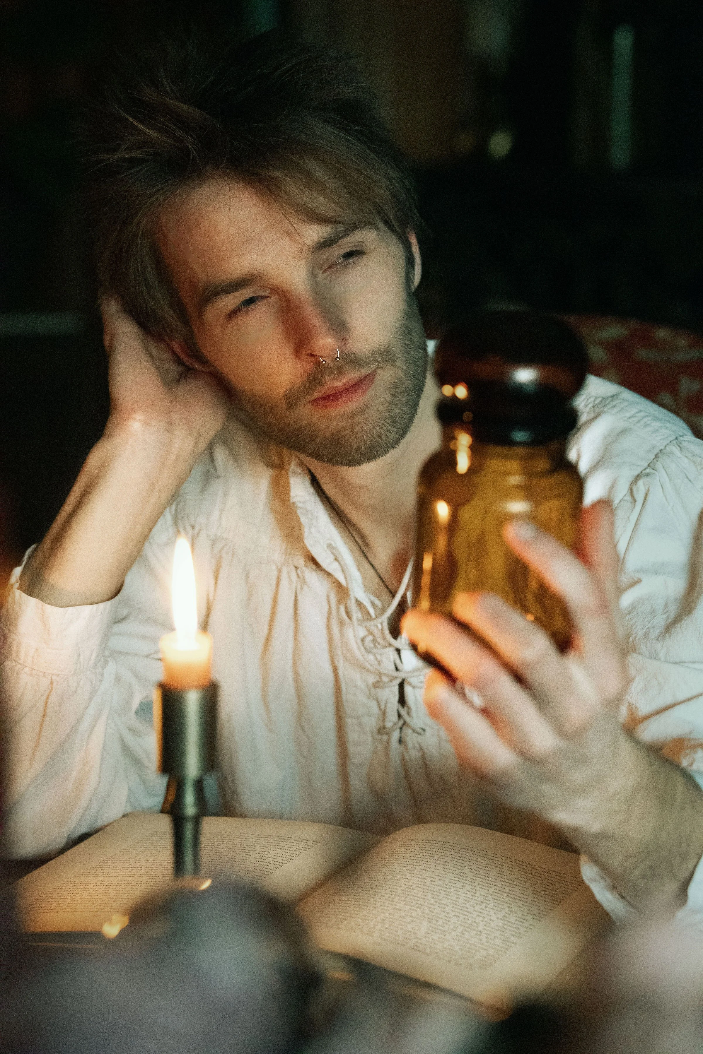 Dreamy fine art portrait of Rico as a scholar reading by candlelight. Painterly fantasy photography inspired by folklore and classical paintings, featuring books, glass bottles and warm light. Moody, romantic storytelling imagery in a fine art studio