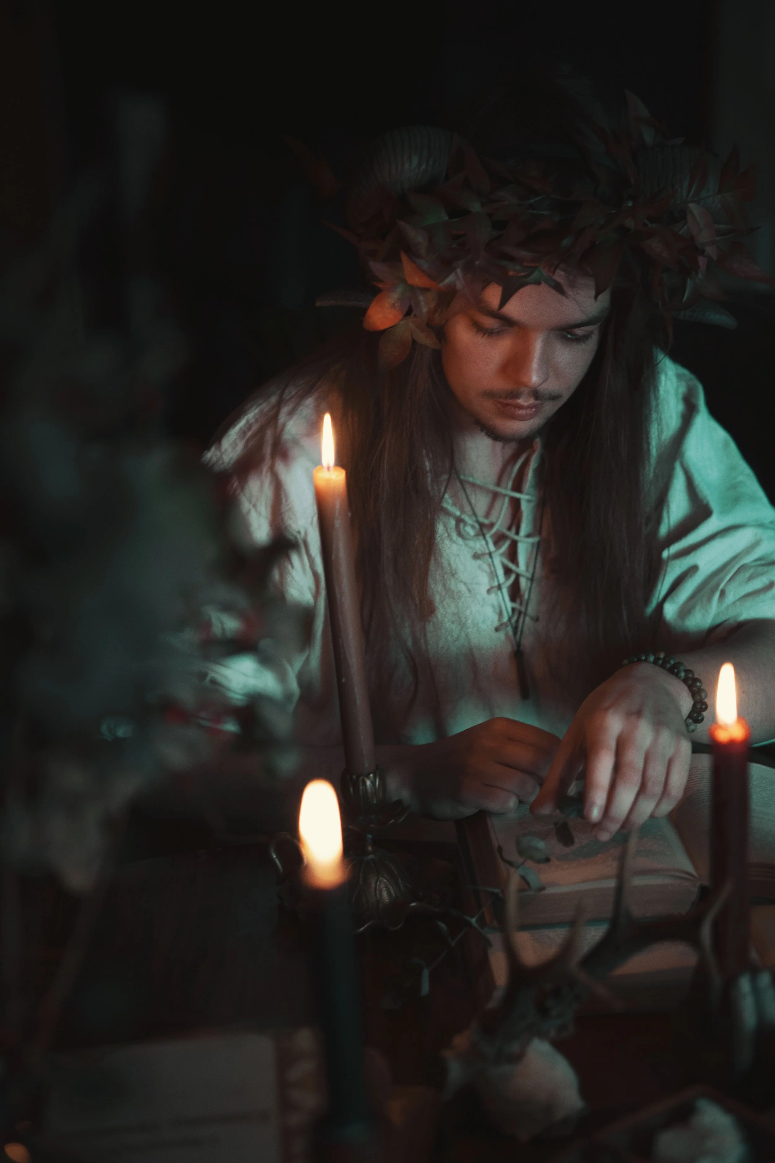 Person with long hair and a laurel wreath reads a book by candlelight.