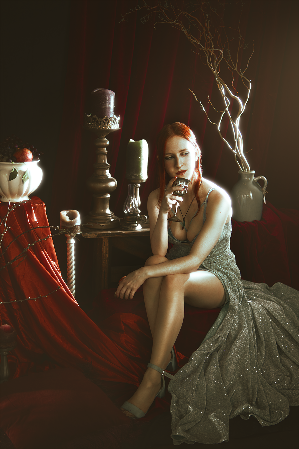 Persephone inspired dark goddess cosplay portrait with pomegranate, red velvet and candlelight. Fine art fantasy photography based on Greek mythology, featuring rich colors and a moody, storytelling atmosphere.