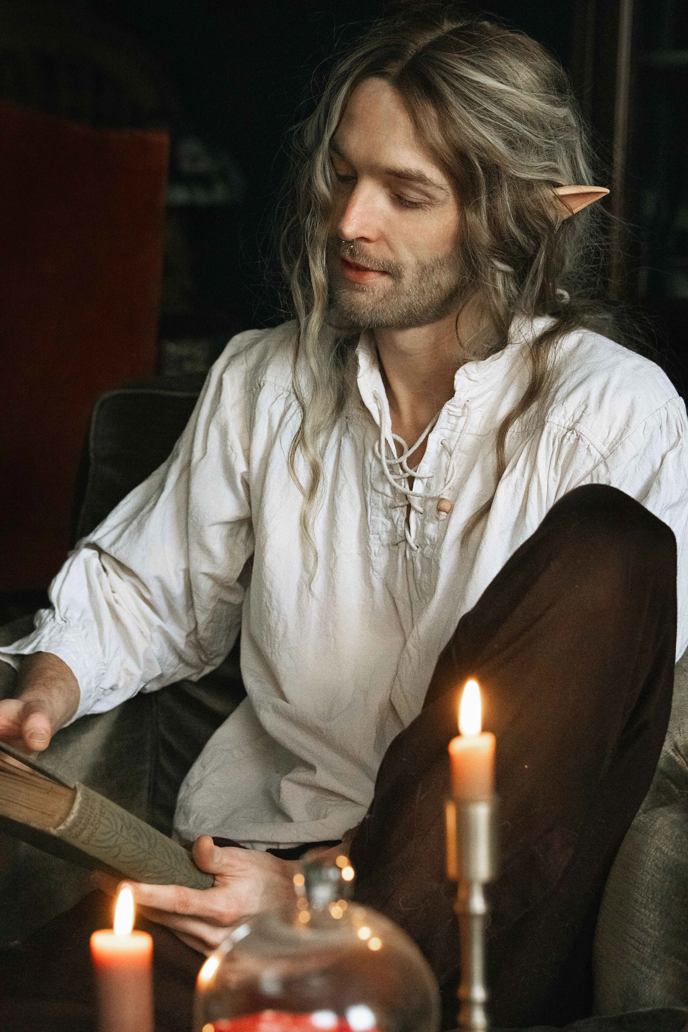 Dreamy fine art portrait of Rico as a scholar reading by candlelight. Painterly fantasy photography inspired by folklore and classical paintings, featuring books, glass bottles and warm light. Moody, romantic storytelling imagery in a fine art studio