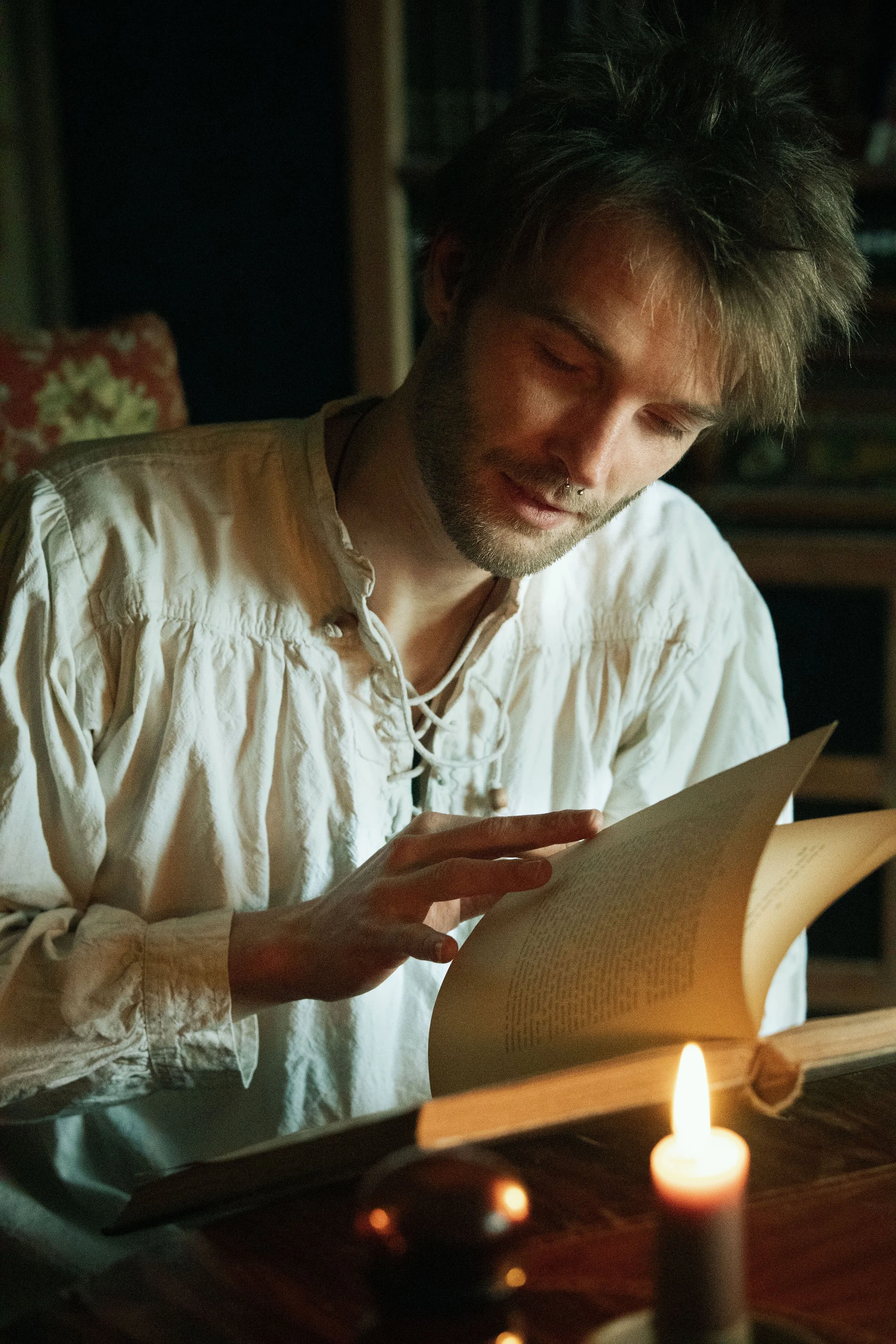 Dreamy fine art portrait of Rico as a scholar reading by candlelight. Painterly fantasy photography inspired by folklore and classical paintings, featuring books, glass bottles and warm light. Moody, romantic storytelling imagery in a fine art studio