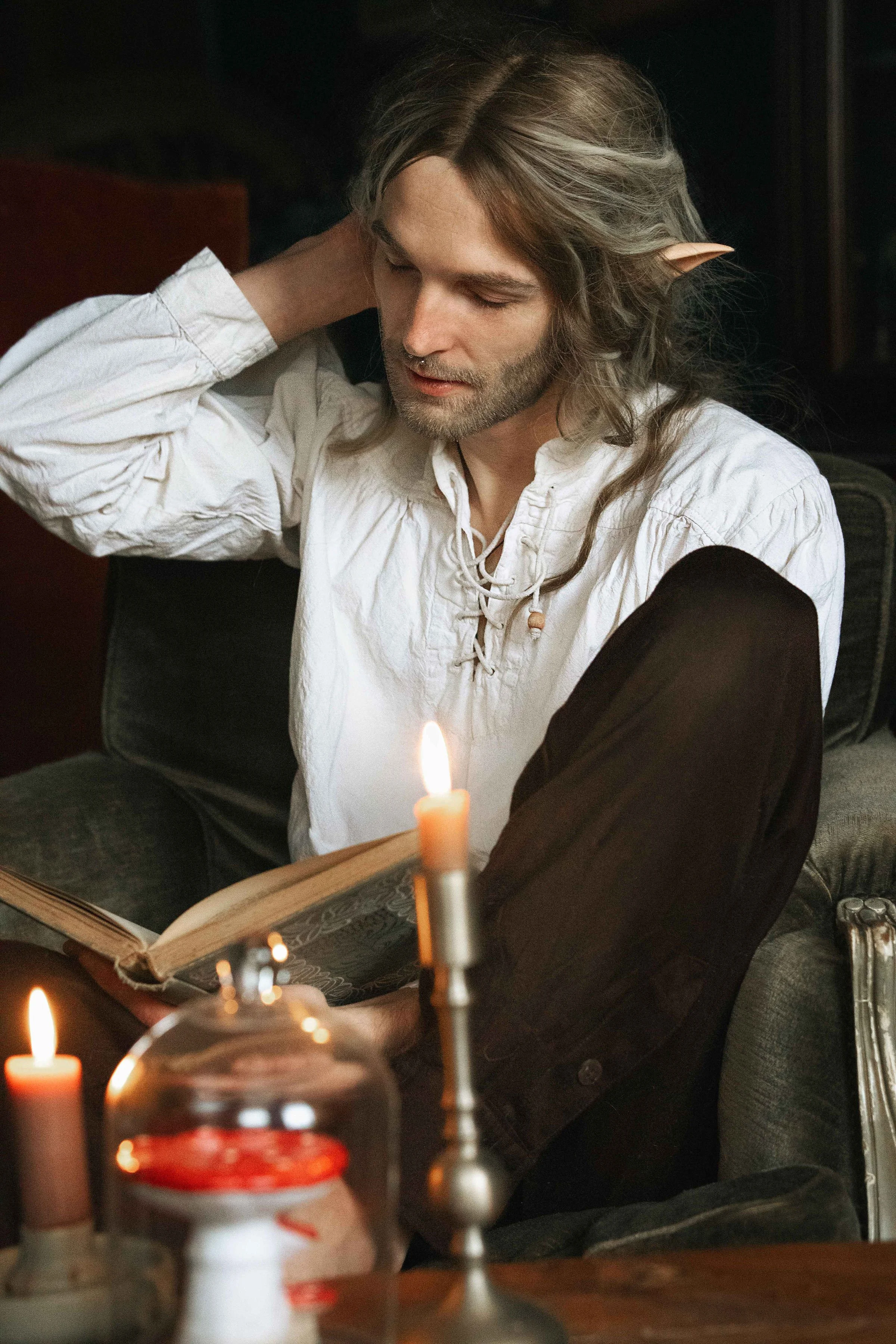 Dreamy fine art portrait of Rico as a scholar reading by candlelight. Painterly fantasy photography inspired by folklore and classical paintings, featuring books, glass bottles and warm light. Moody, romantic storytelling imagery in a fine art studio