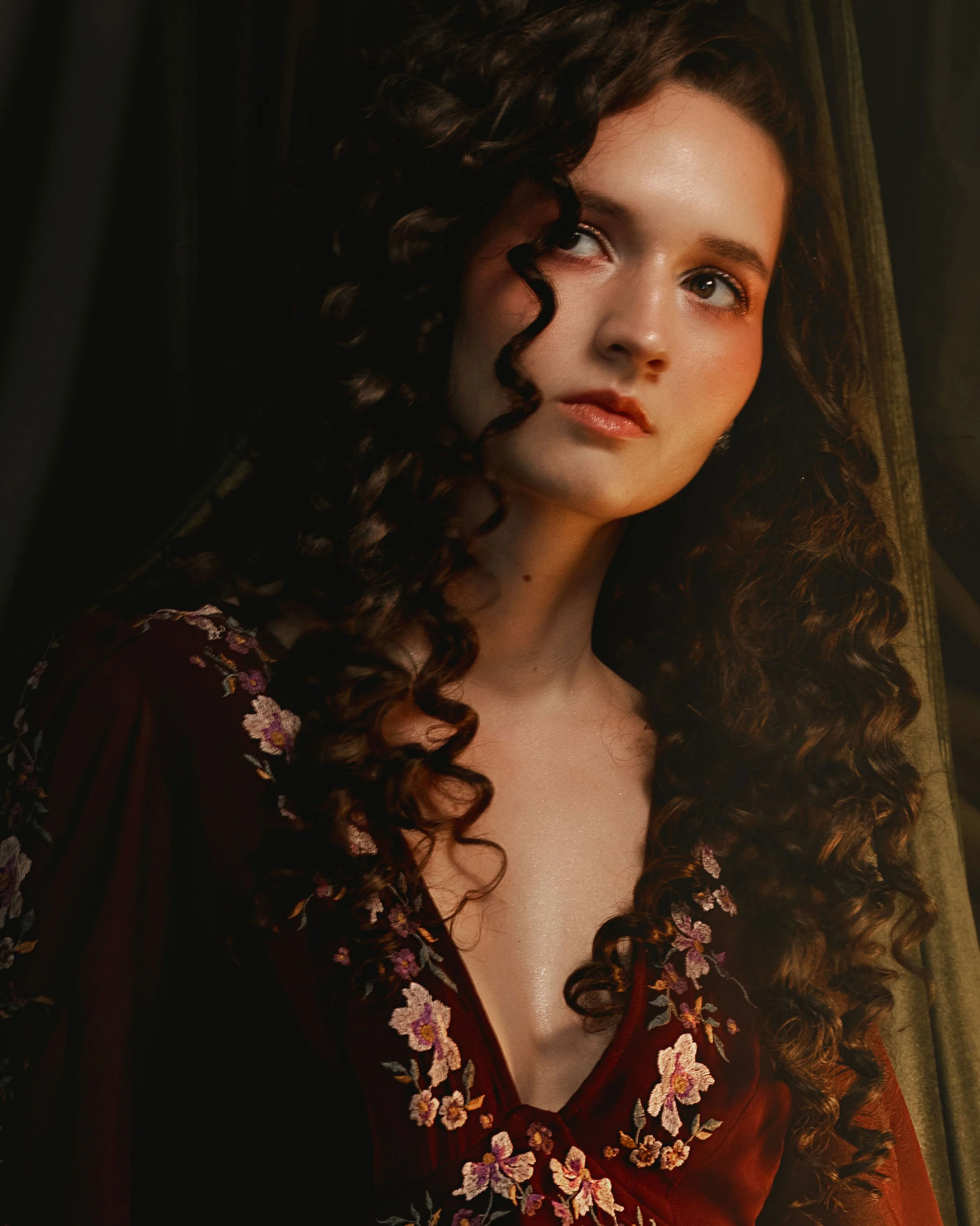 Dark romantic fine art portrait of a woman in deep red and violet tones with candlelight and vintage styling. Painterly fantasy photography inspired by baroque art and historical fashion, featuring rich fabrics and soft dramatic light.
