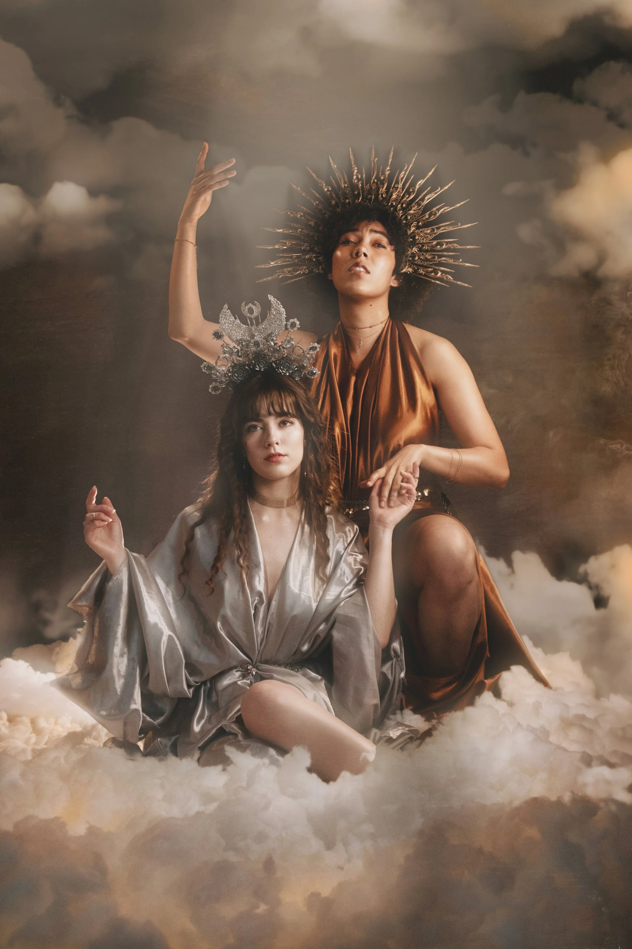 Fine art fantasy portrait of sun and moon goddesses with celestial crowns, clouds and dramatic light. Mythology inspired photography with golden and silver tones, painterly style and dreamy storytelling atmosphere.
