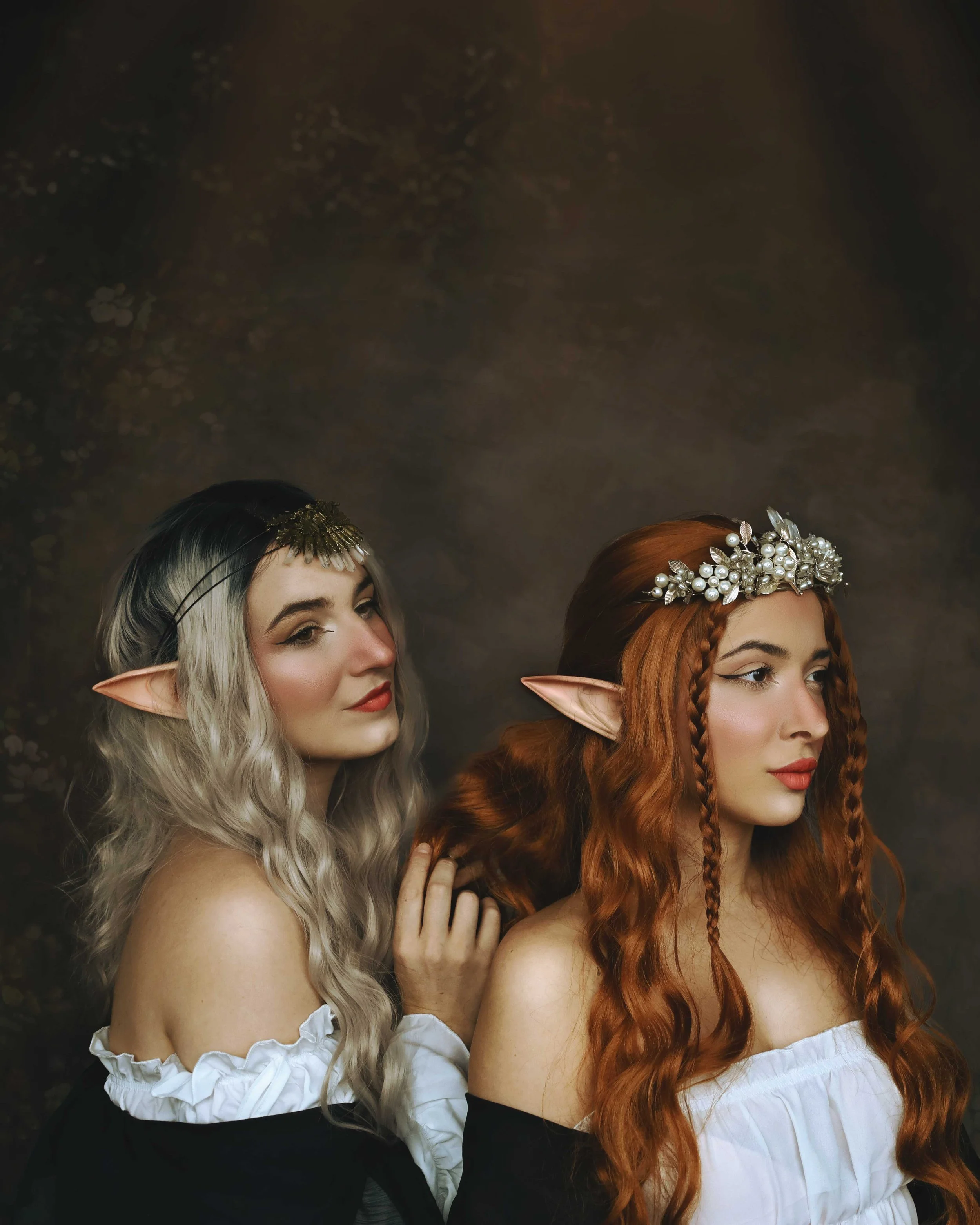 Two women dressed as elves with pointed ears and decorative headdresses, wearing fantasy-style outfits.