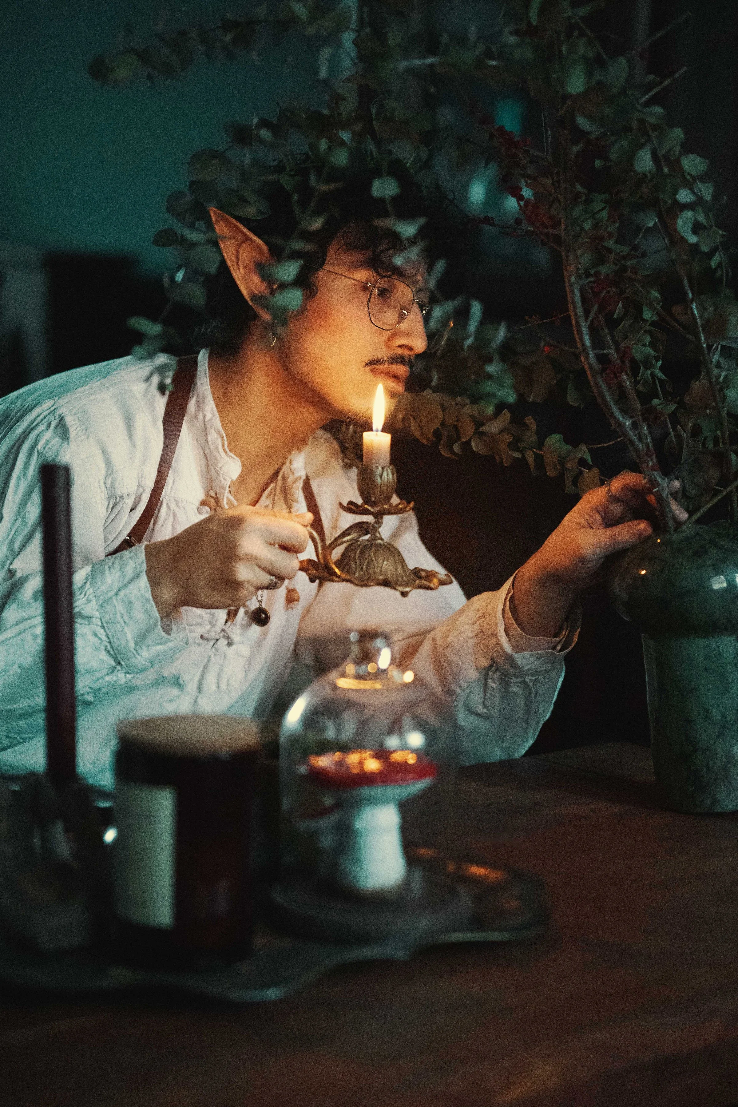 Dreamy fine art portrait of Dewa as a folkloric alchemist, surrounded by glass bottles, herbs and candlelight. Painterly fantasy photography inspired by historical apothecaries and storytelling portraiture. Studio shoot in the Netherlands.