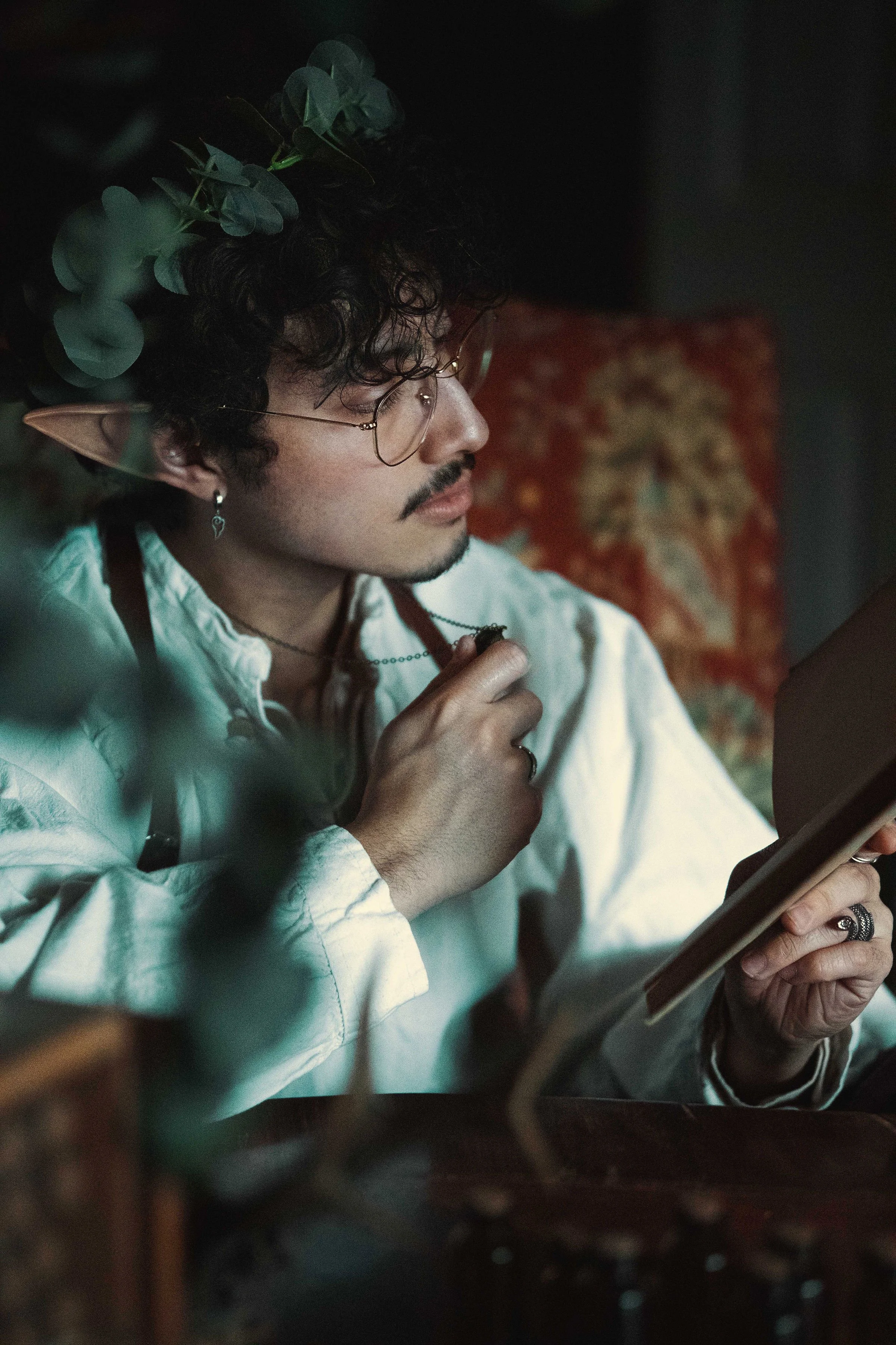 Dreamy fine art portrait of Dewa as a folkloric alchemist, surrounded by glass bottles, herbs and candlelight. Painterly fantasy photography inspired by historical apothecaries and storytelling portraiture. Studio shoot in the Netherlands.