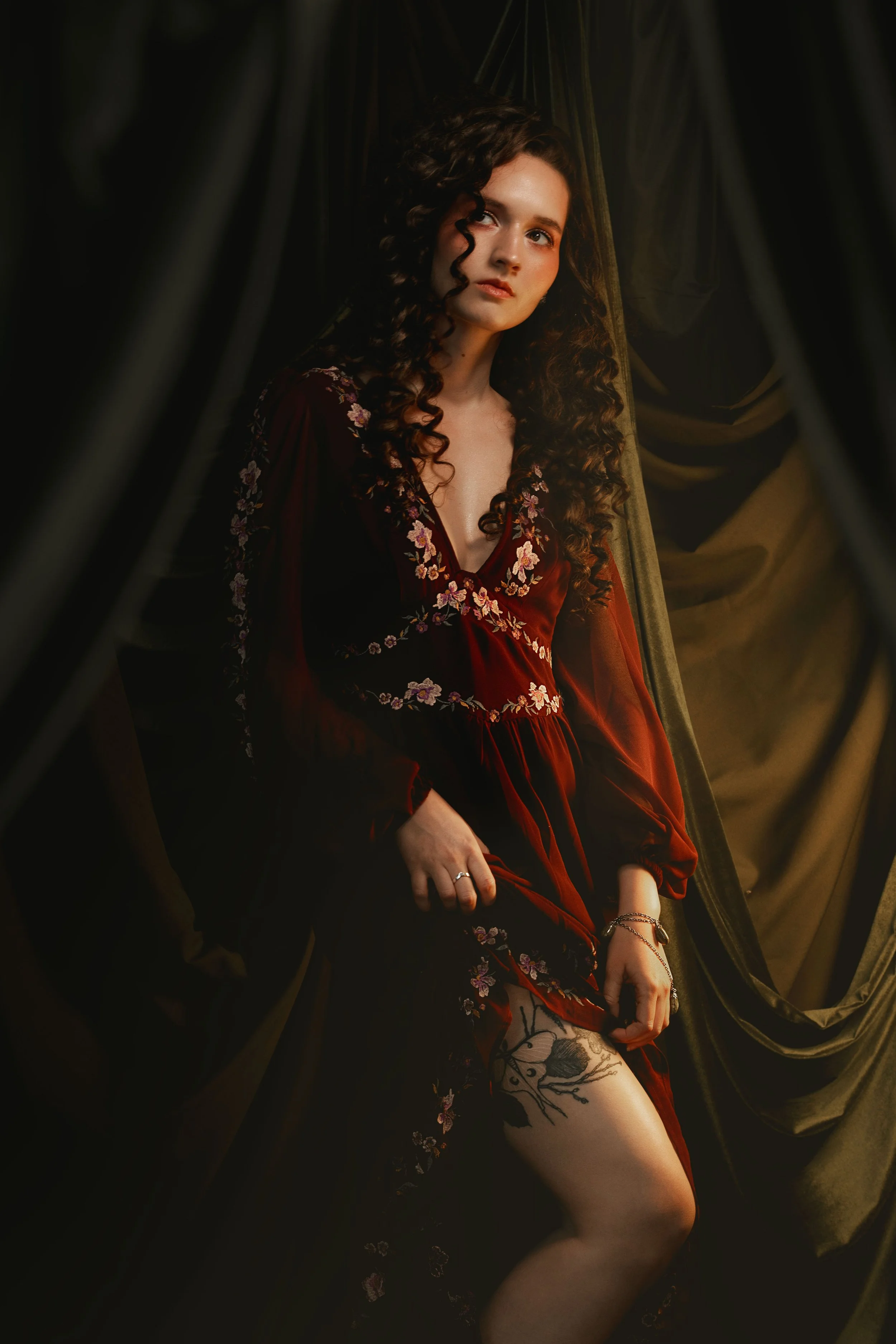 Dark romantic fine art portrait of a woman in deep red and violet tones with candlelight and vintage styling. Painterly fantasy photography inspired by baroque art and historical fashion, featuring rich fabrics and soft dramatic light.