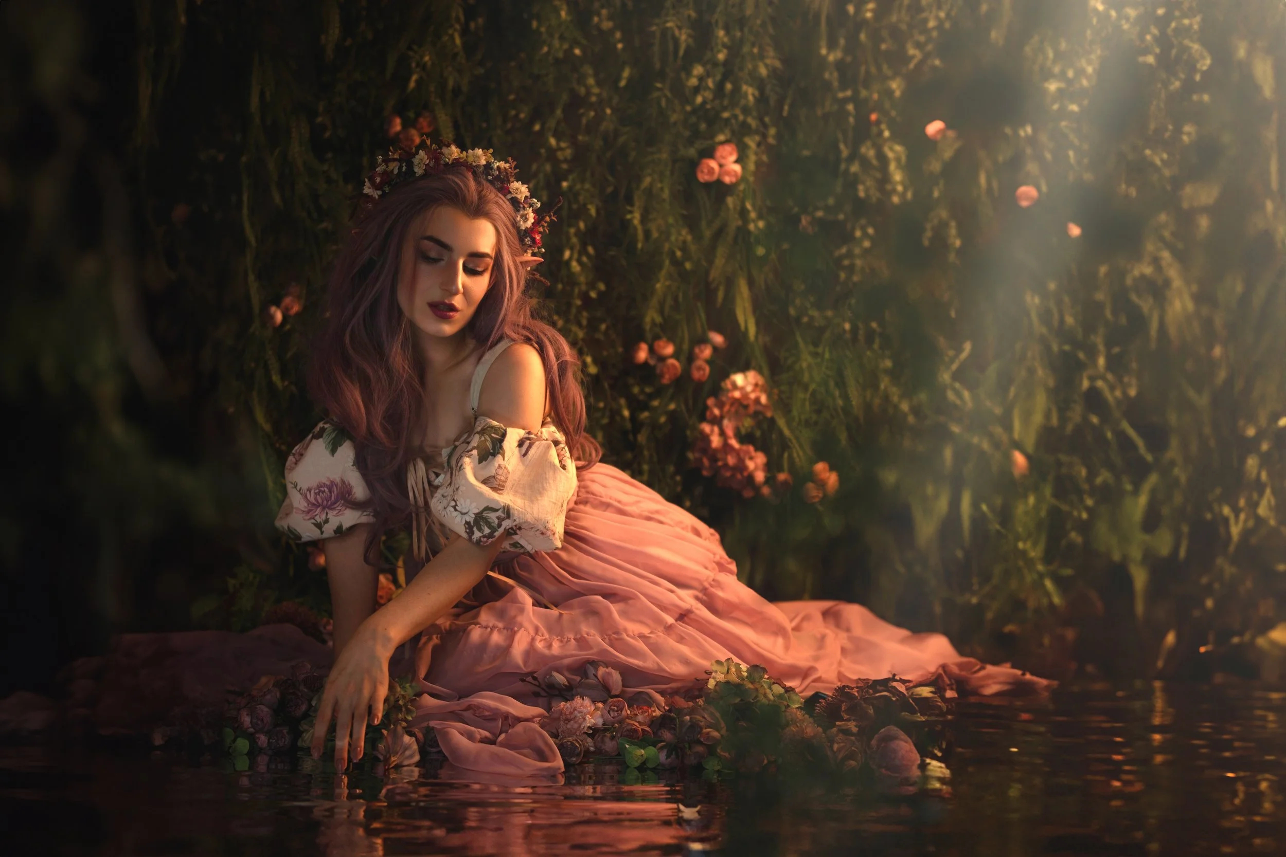 A woman in a pink dress sitting by a water's edge, surrounded by foliage and flowers, with a dreamy, ethereal atmosphere.