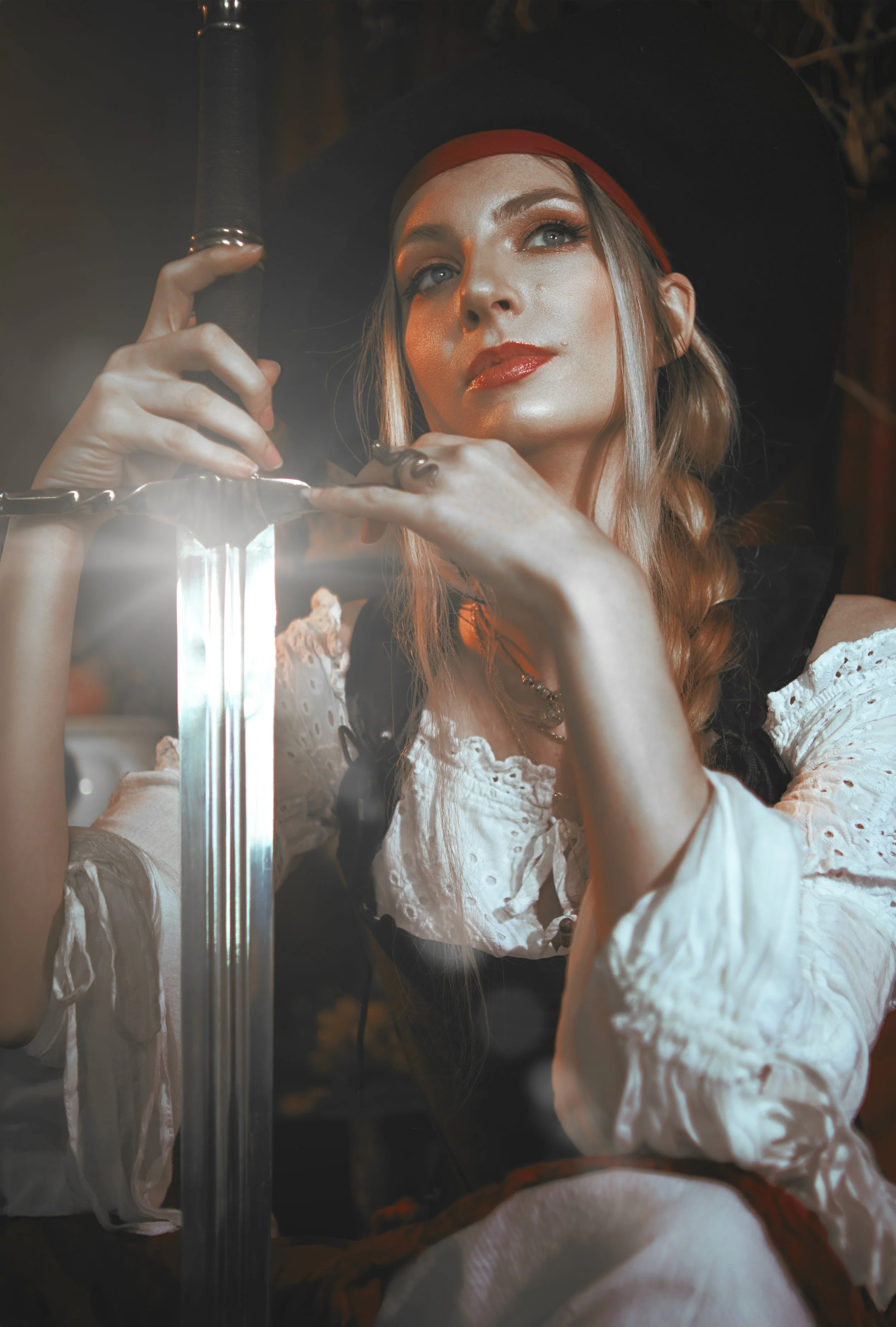 Pirate inspired cosplay portrait with sword and historical styling. Fine art fantasy photography influenced by seafaring adventures and vintage aesthetics, featuring warm light and a cinematic storytelling atmosphere.