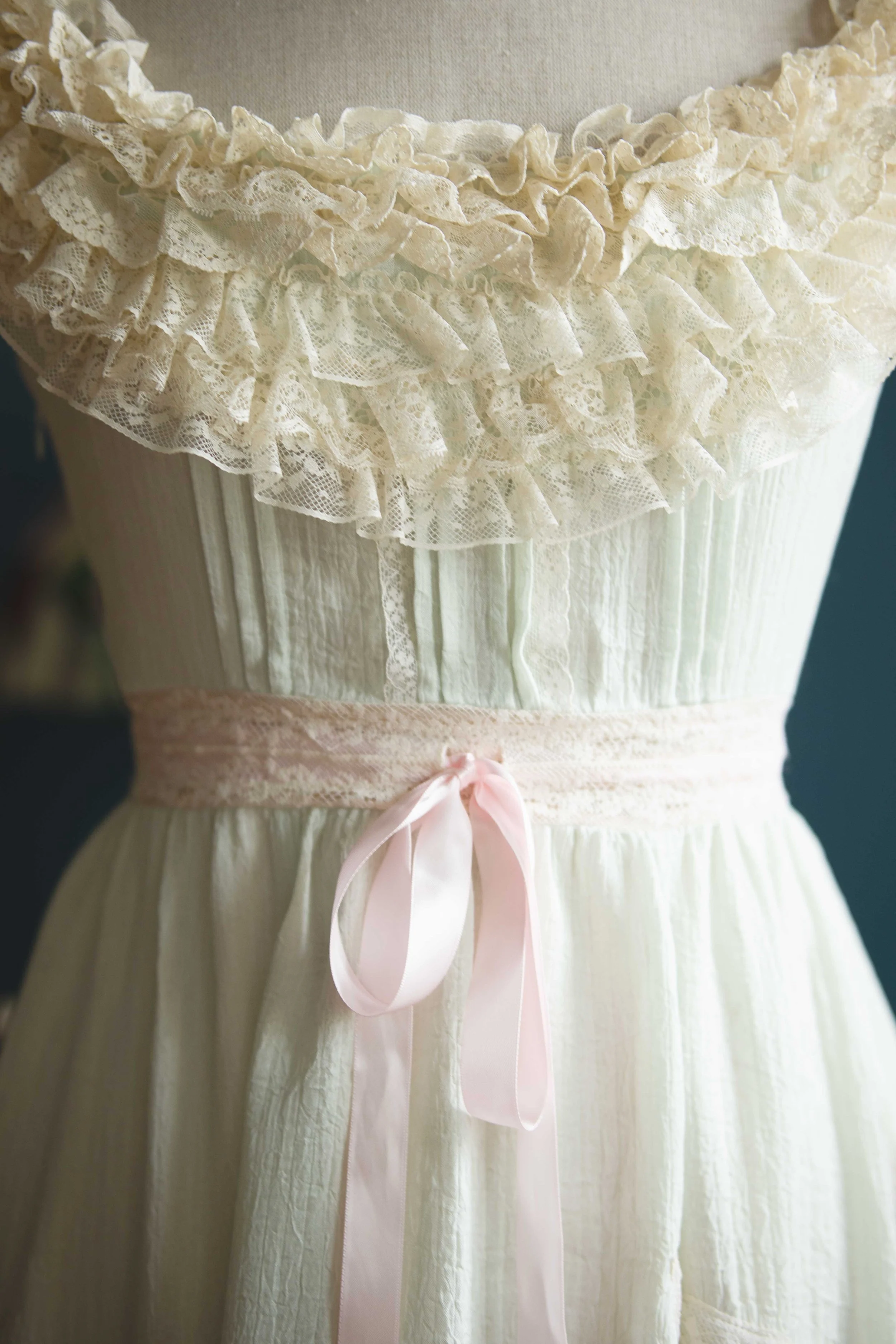 Close-up of a white dress with lace ruffles and a pink satin ribbon belt.