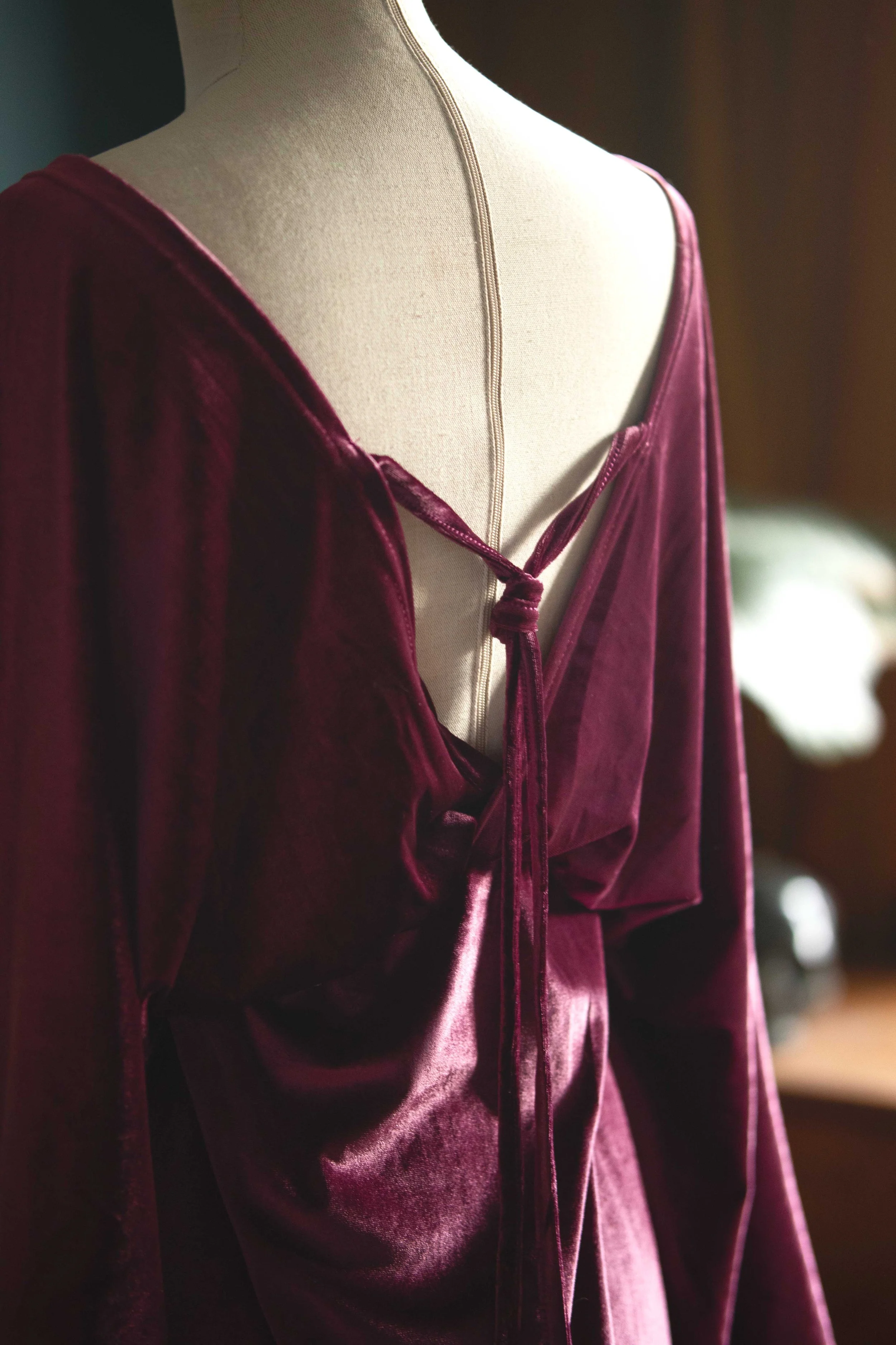 Back view of a maroon velvet dress on a mannequin featuring a tied strap detail.