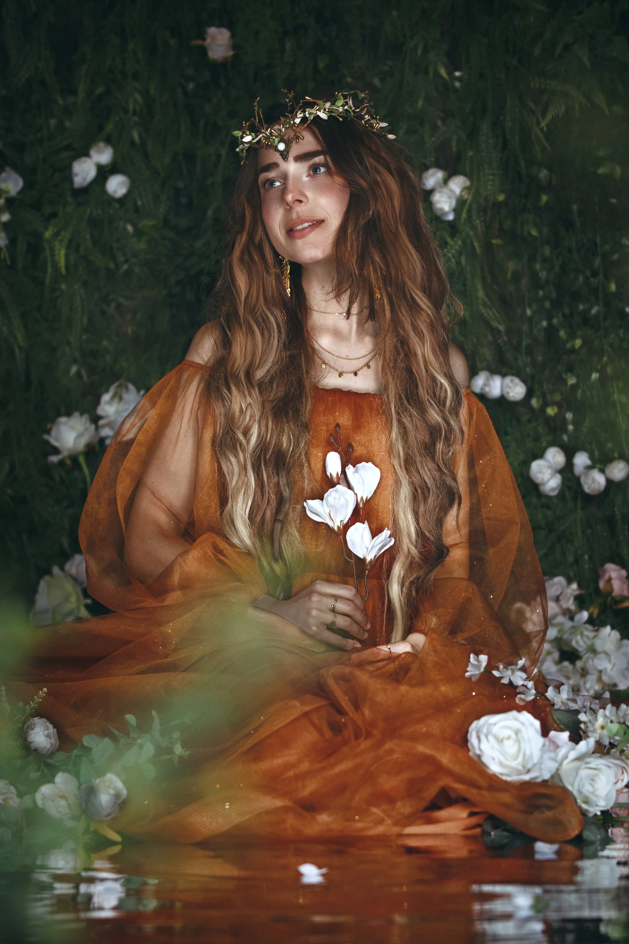 Dreamy fine art portrait of a flower nymph in water surrounded by blossoms and greenery. Ethereal fantasy photography inspired by folklore, mythology and nature. Painterly, romantic imagery with soft light, floral details and storytelling atmosphere.