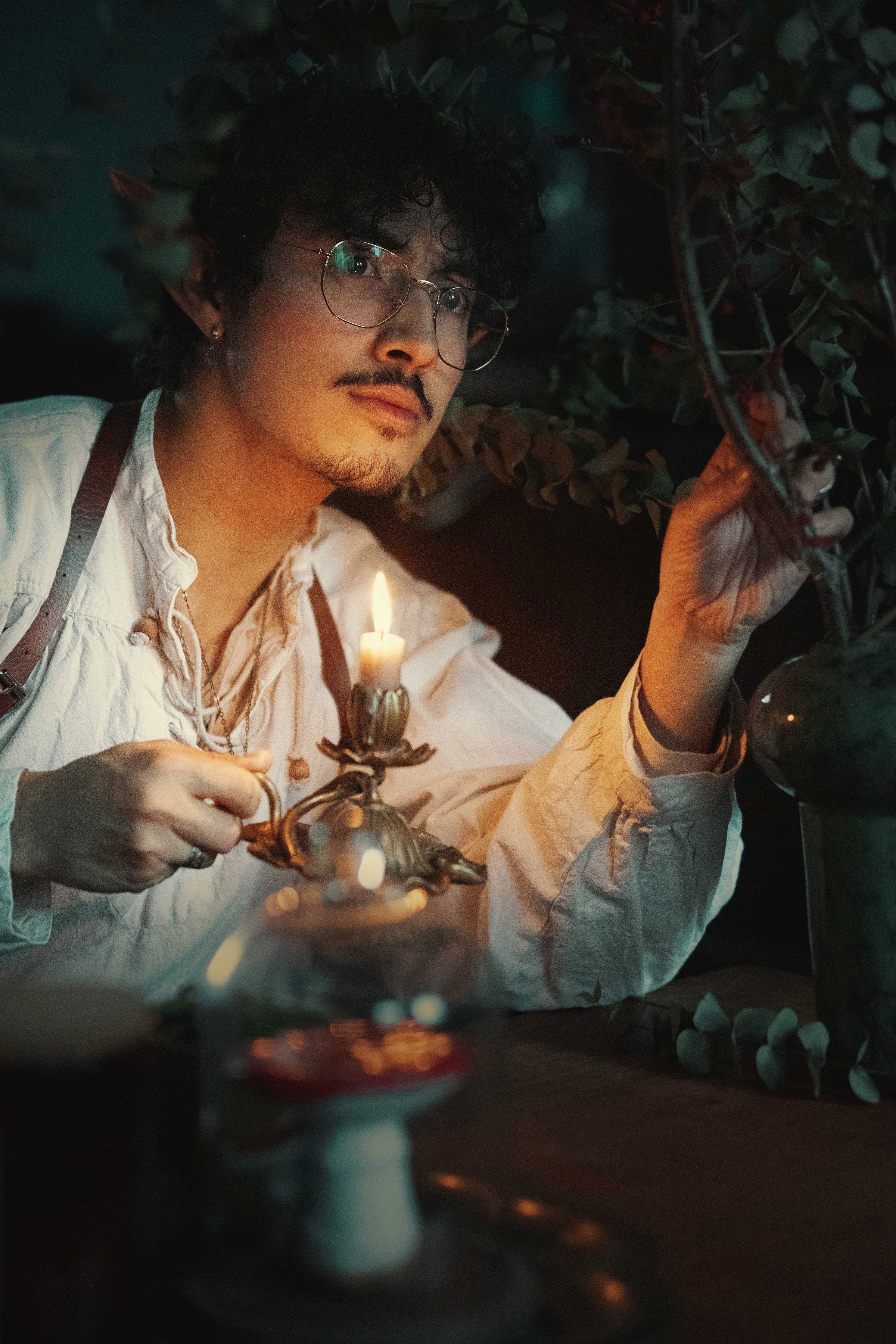 Dreamy fine art portrait of Dewa as a folkloric alchemist, surrounded by glass bottles, herbs and candlelight. Painterly fantasy photography inspired by historical apothecaries and storytelling portraiture. Studio shoot in the Netherlands.