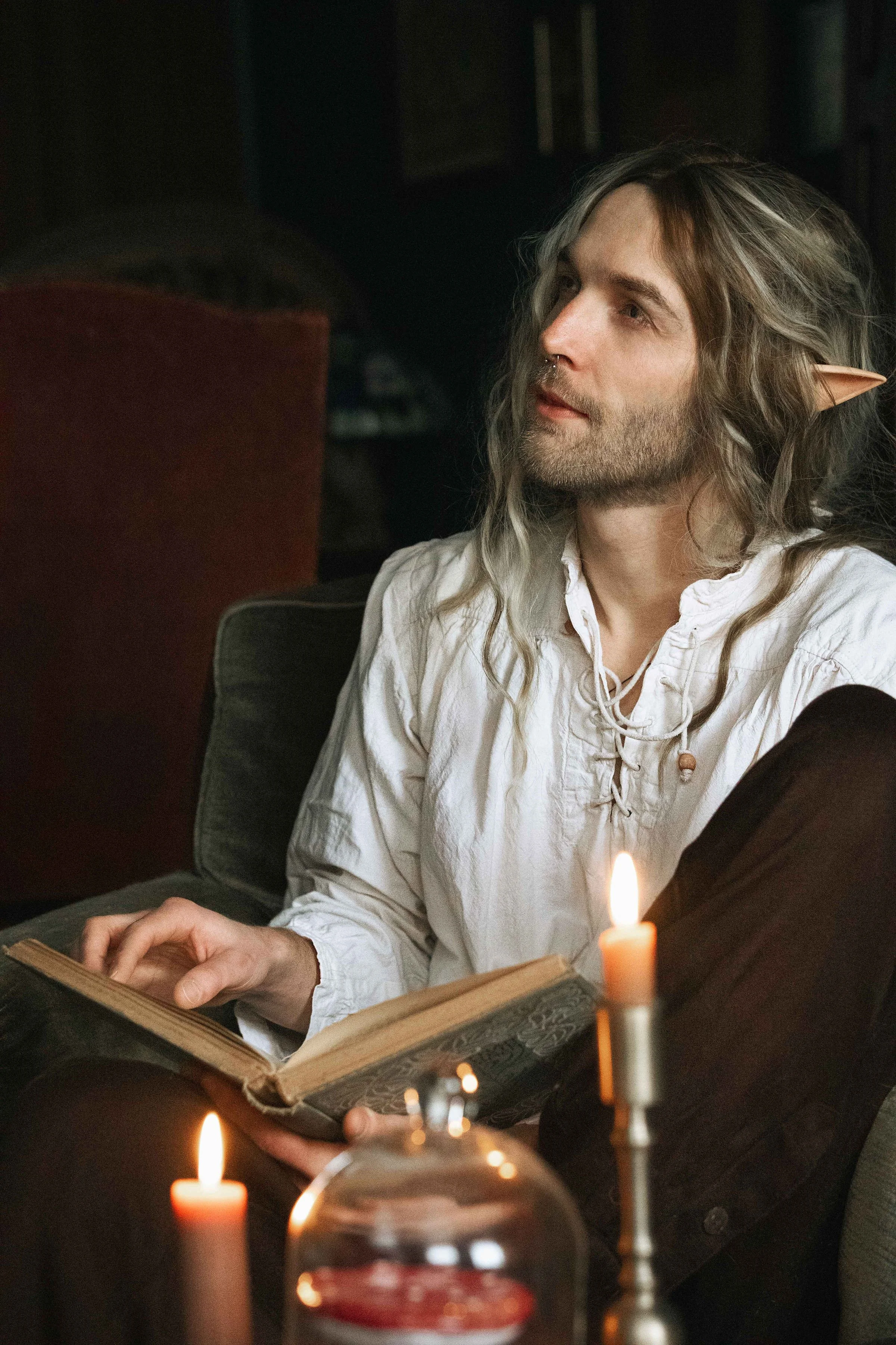 Dreamy fine art portrait of Rico as a scholar reading by candlelight. Painterly fantasy photography inspired by folklore and classical paintings, featuring books, glass bottles and warm light. Moody, romantic storytelling imagery in a fine art studio
