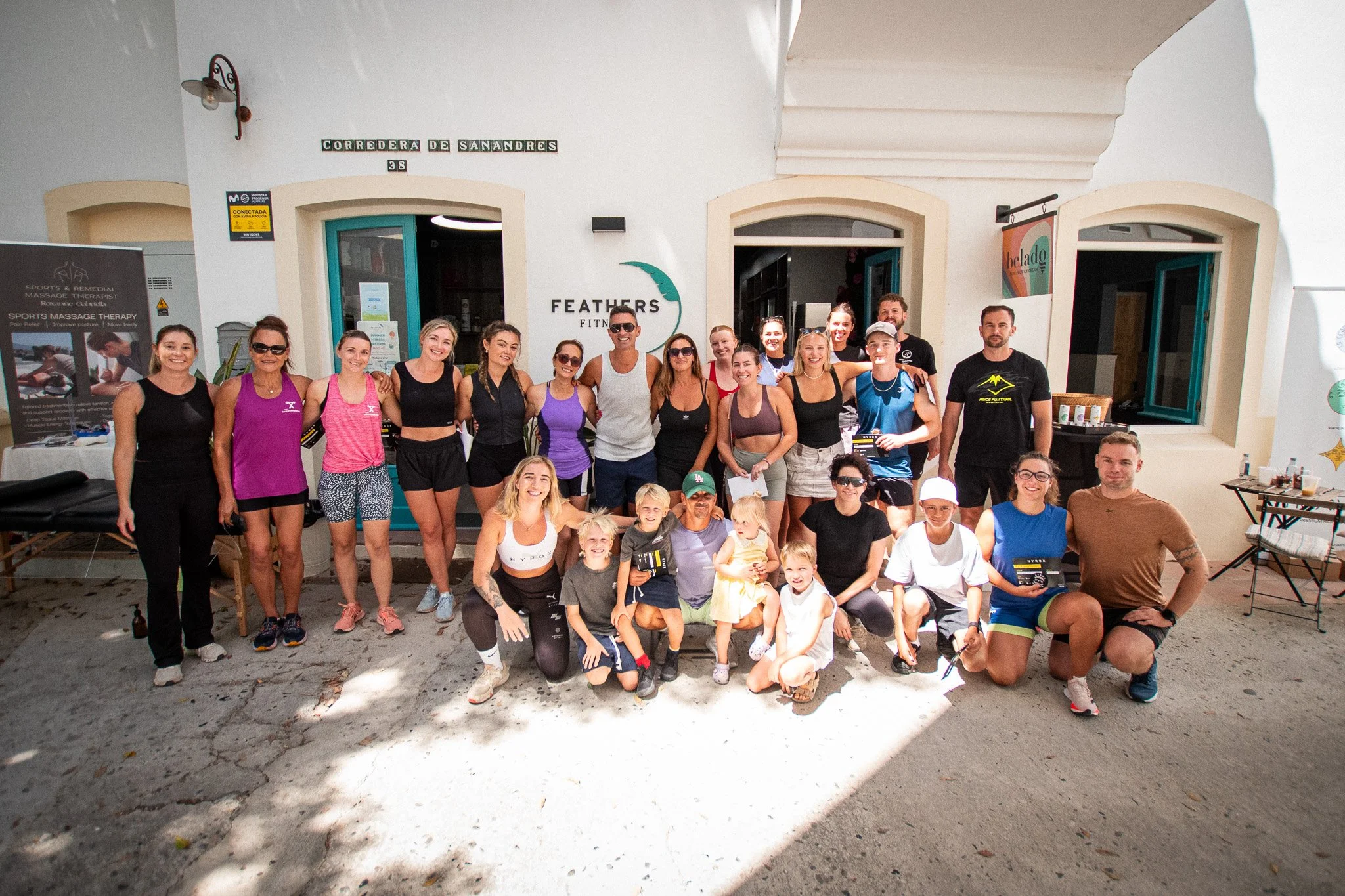 Group of people posing outside a fitness or wellness establishment with sign 'Feathers Fitness' on the wall behind them.