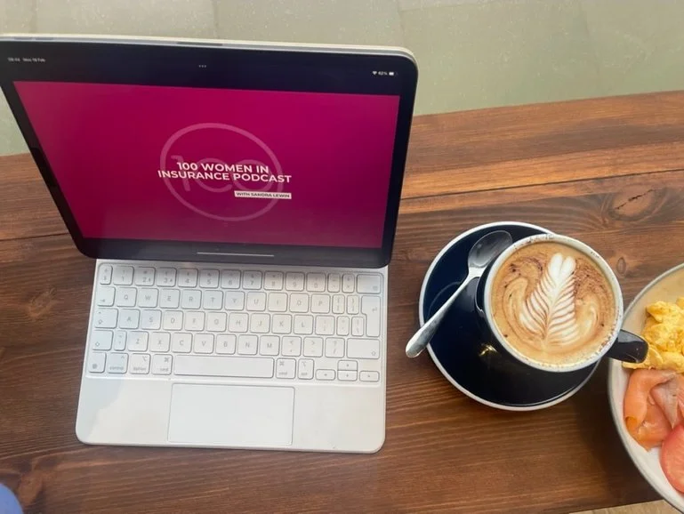 Open laptop with the 100 Women in Insurance podcast logo on the screen, the laptop is next to a latte