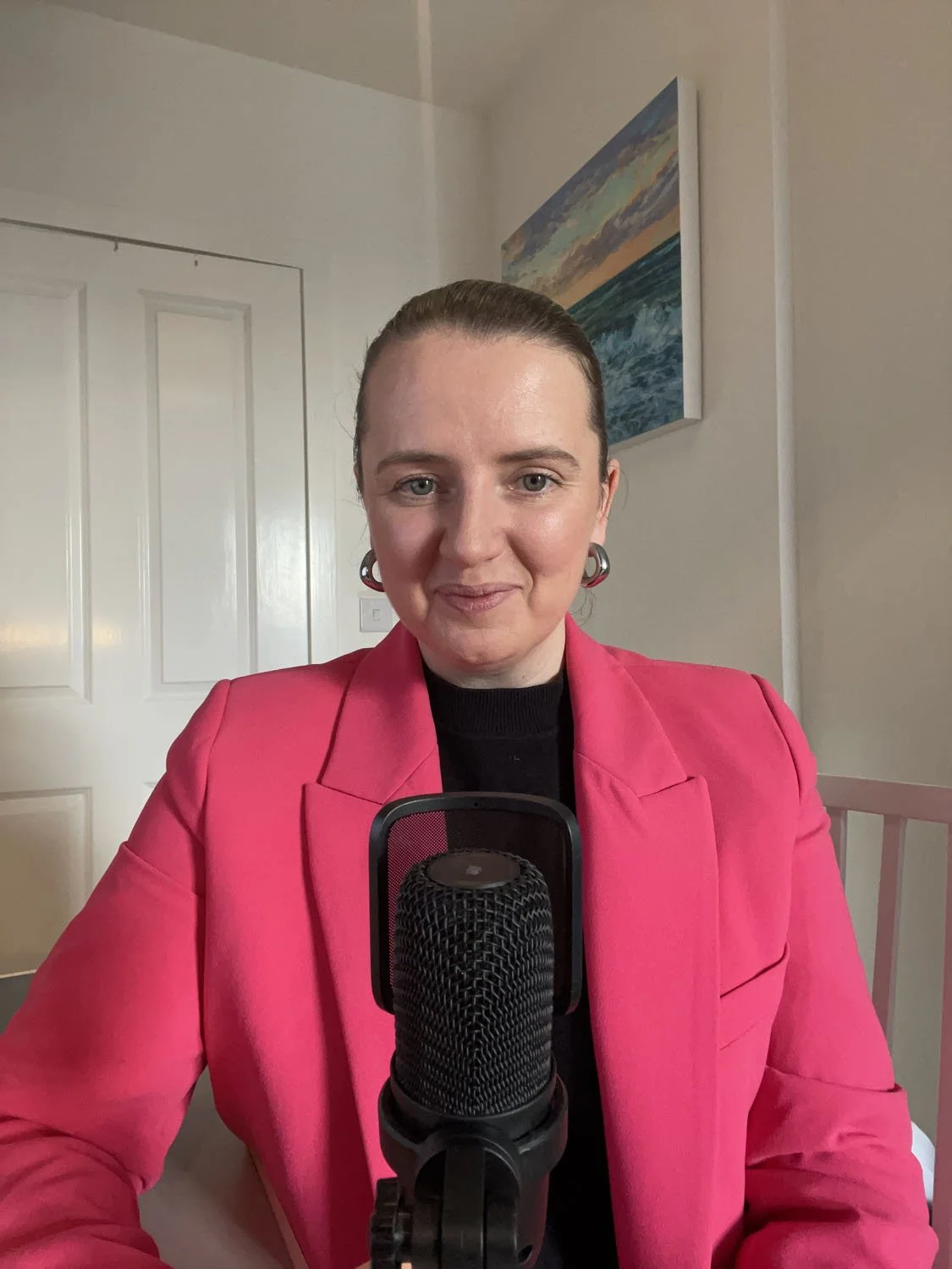 Podcast host Sandra wearing pink blazer while sitting in front of microphone