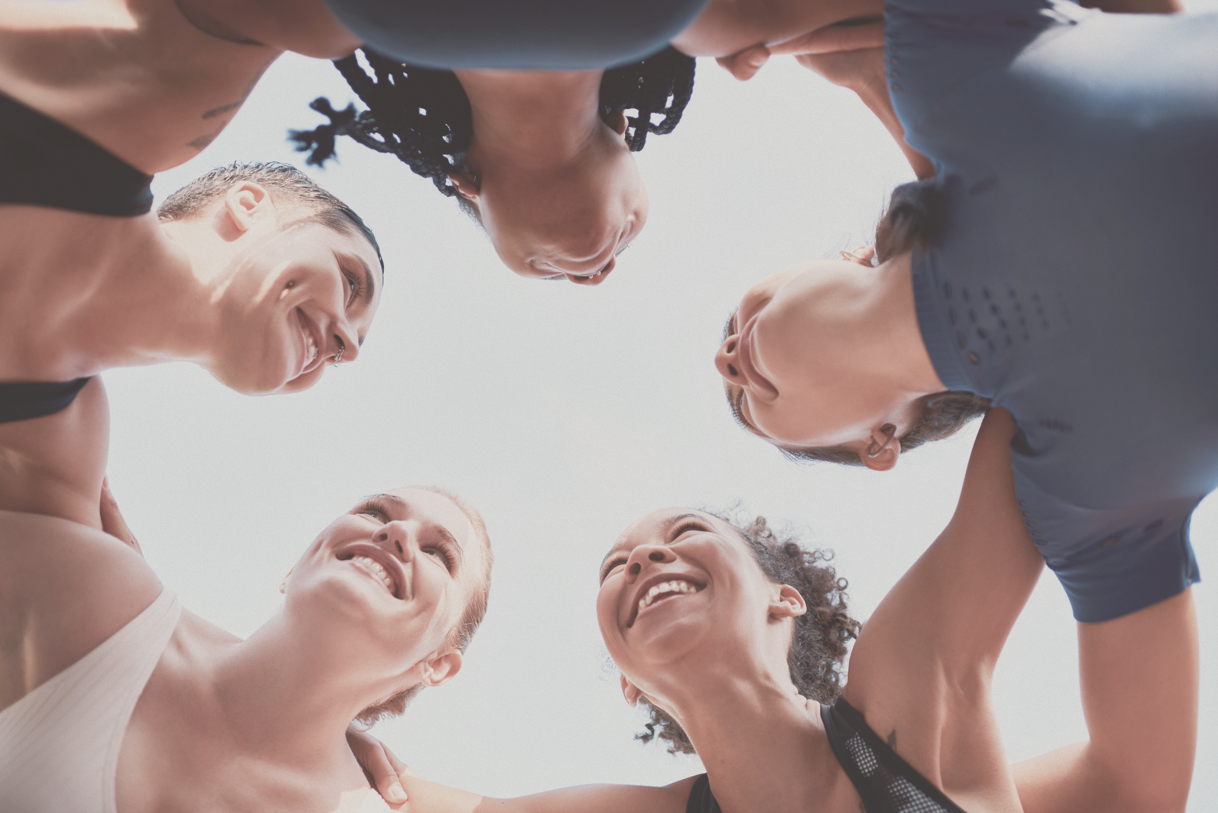 Grupo de cinco personas sonriendo y mostrando sus rostros desde abajo, formando un círculo con sus cabezas juntas.