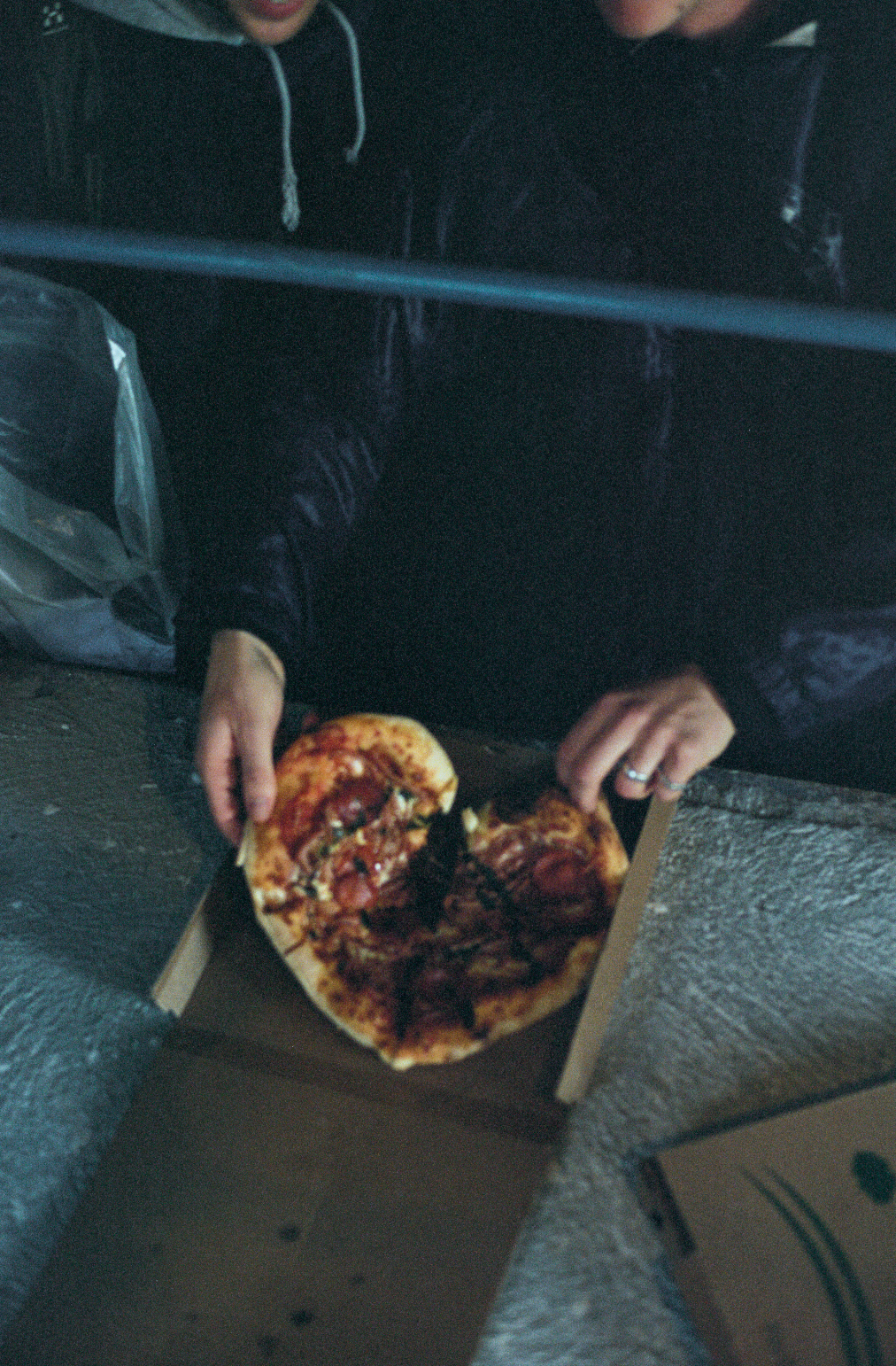 Person holding a pizza with pepperoni and toppings in a cardboard box.