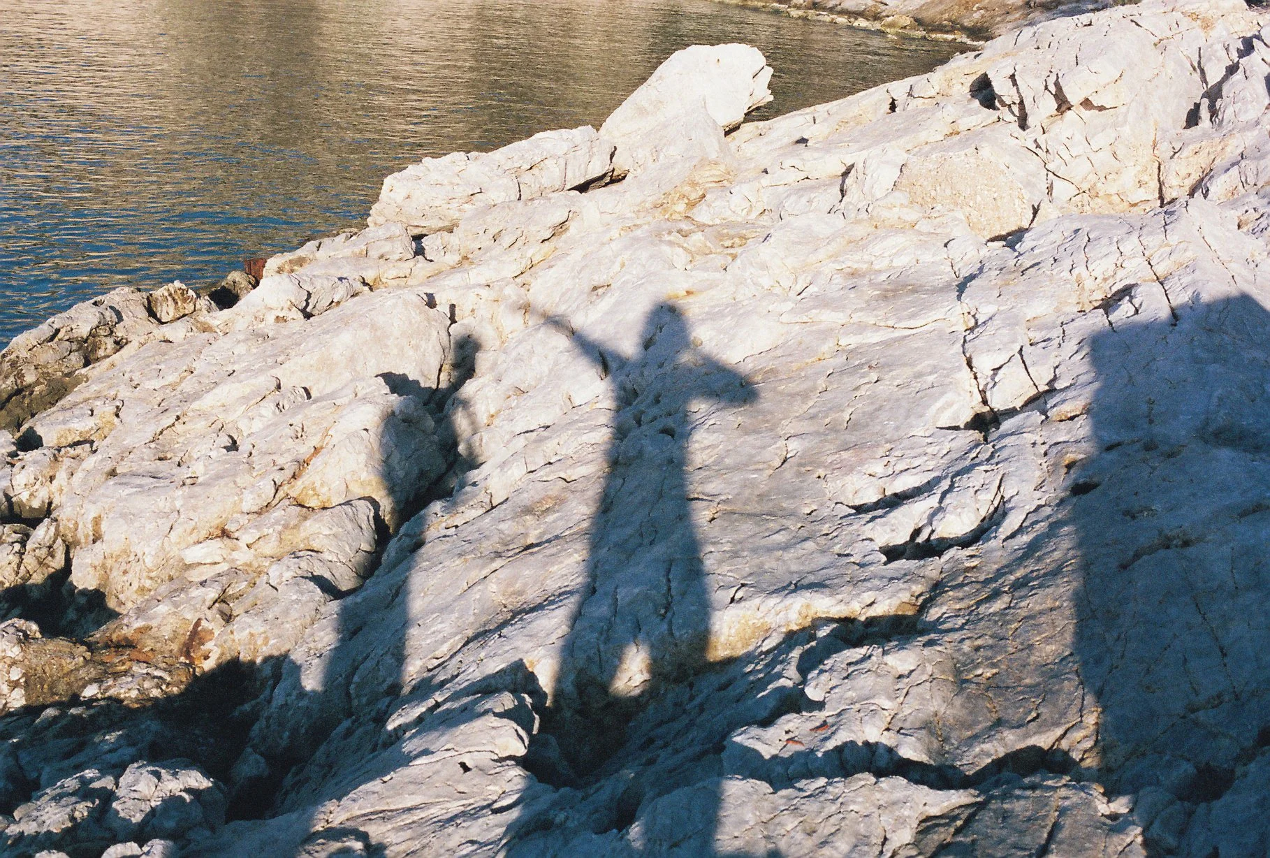 Large white rocks along a body of water with the shadow of a person and butterfly in the foreground