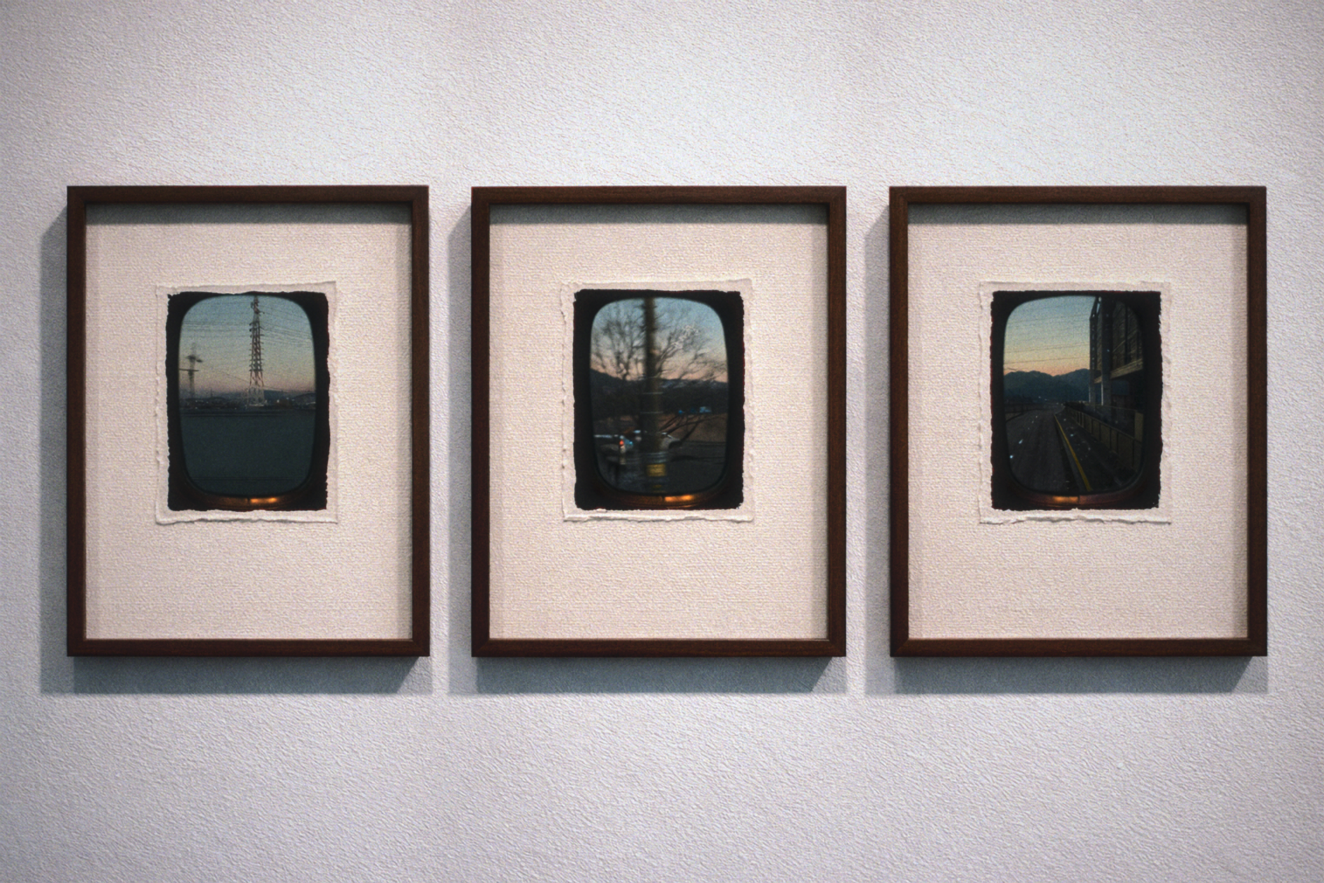 Three framed photographs of views seen through airplane windows are mounted on a wall. The images depict industrial and rural landscapes with power lines, trees, and mountains.