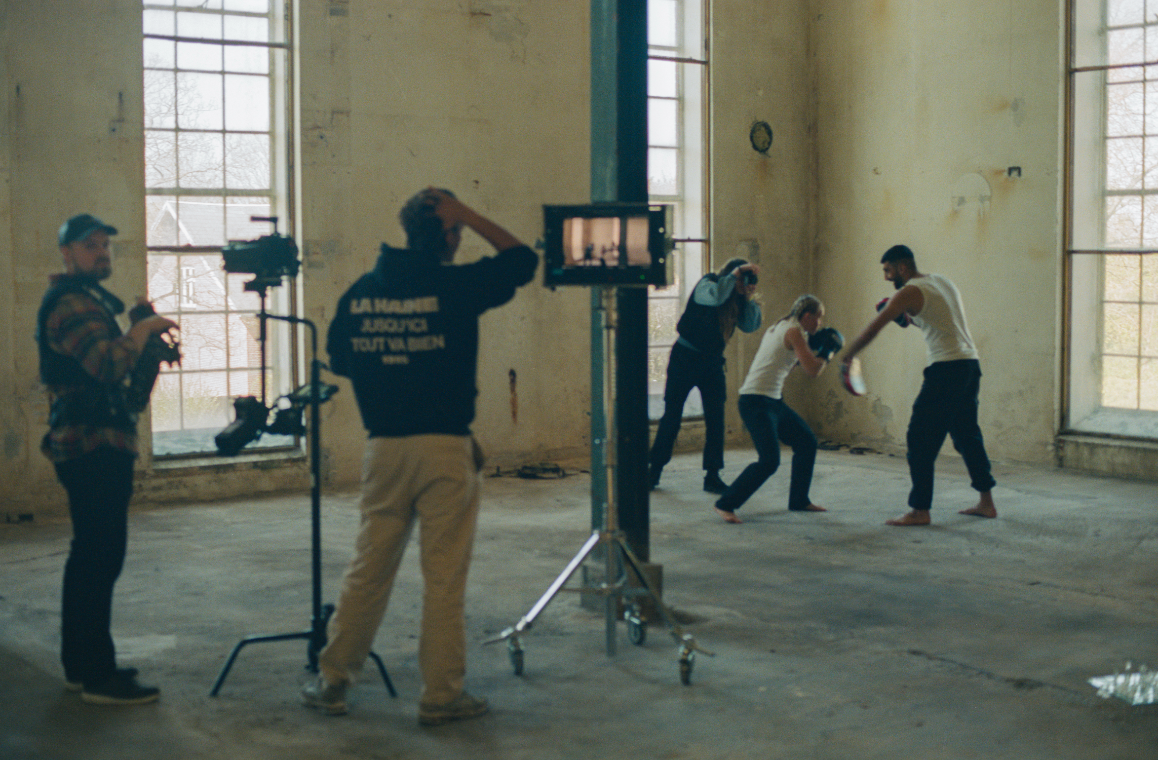 A group of people practicing boxing in a spacious, industrial-style room with large windows and beige walls.