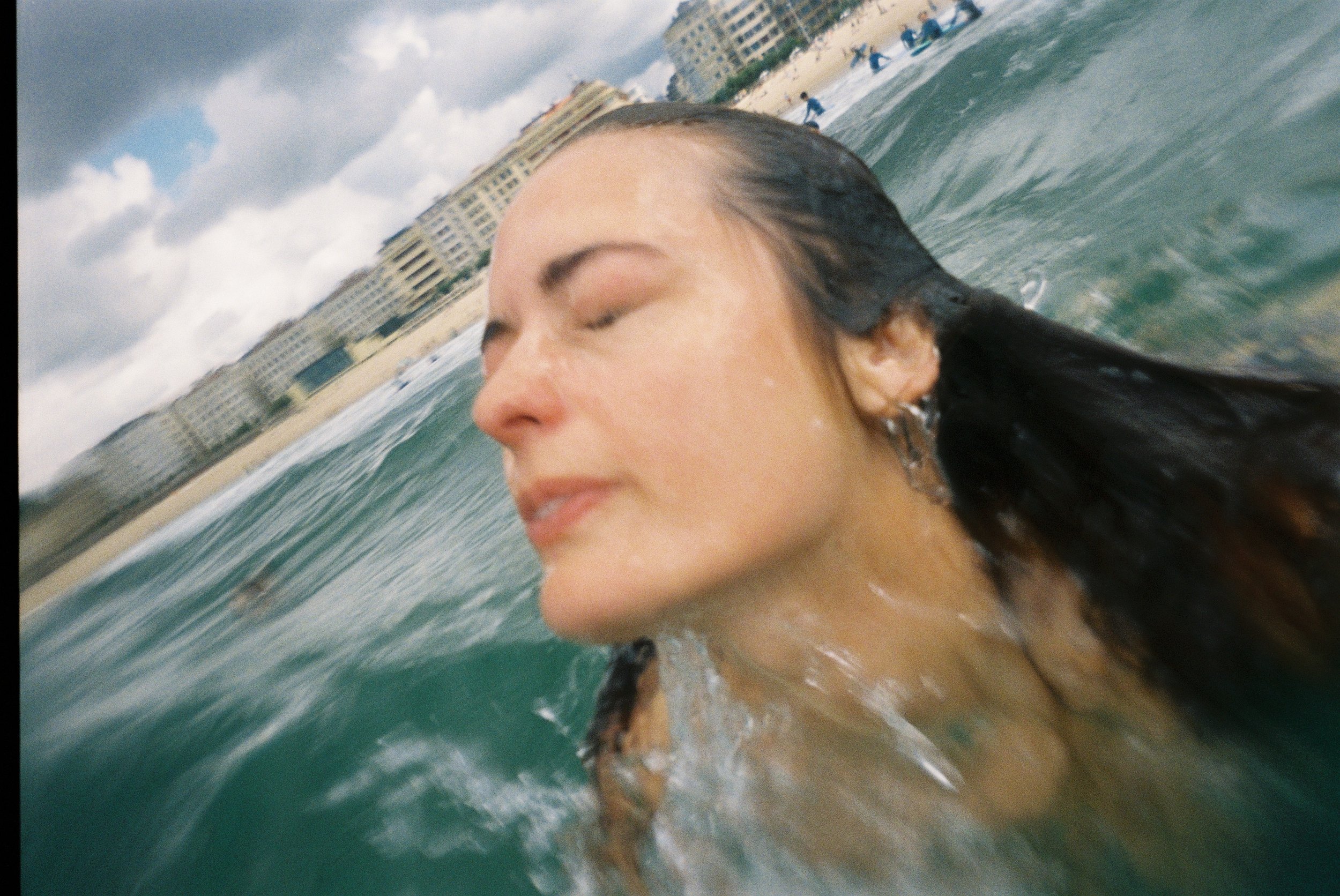 A woman with wet hair with eyes closed, enjoying the ocean waves at the beach during overcast weather.