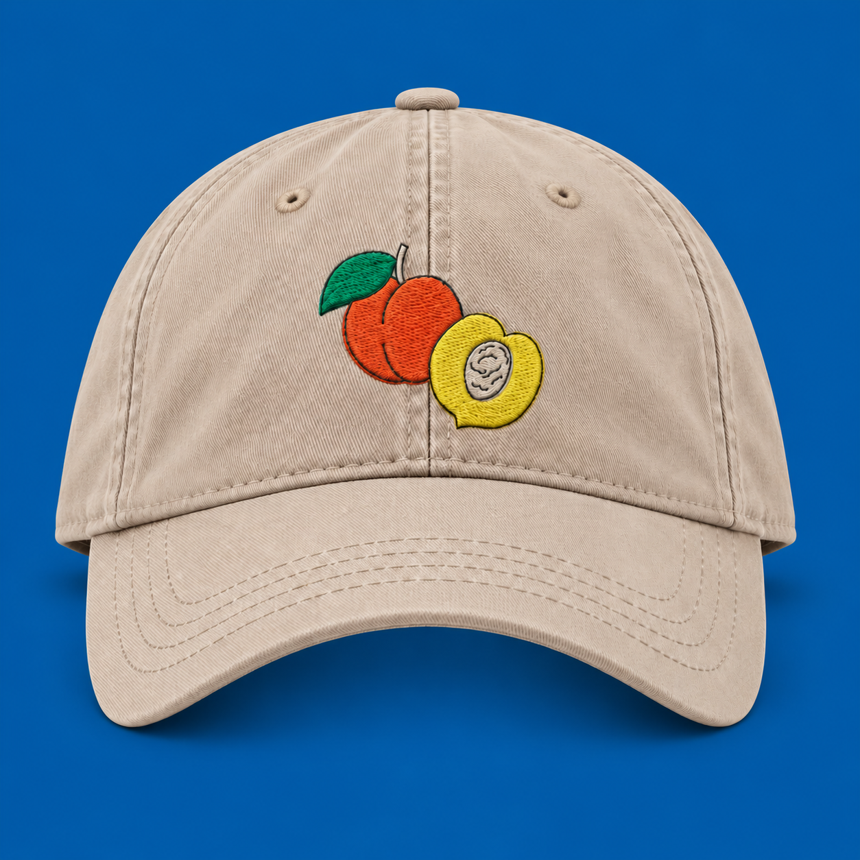 Sand organic cotton cap with embroidered peaches on a blue background.