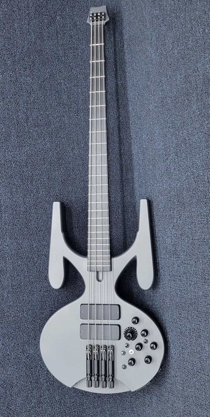 Gray futuristic bass guitar with unique body design, four strings, and multiple control knobs, resting on a blue textured surface.