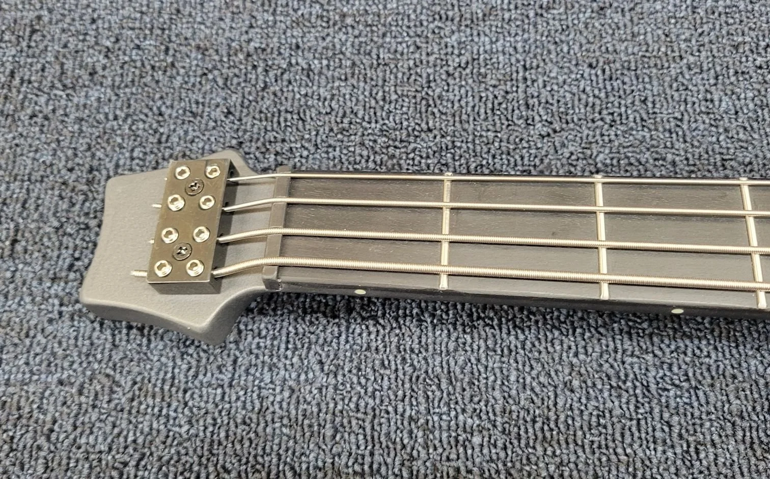 Close-up of a silver musical instrument headstock with four strings and tuning peg screws.