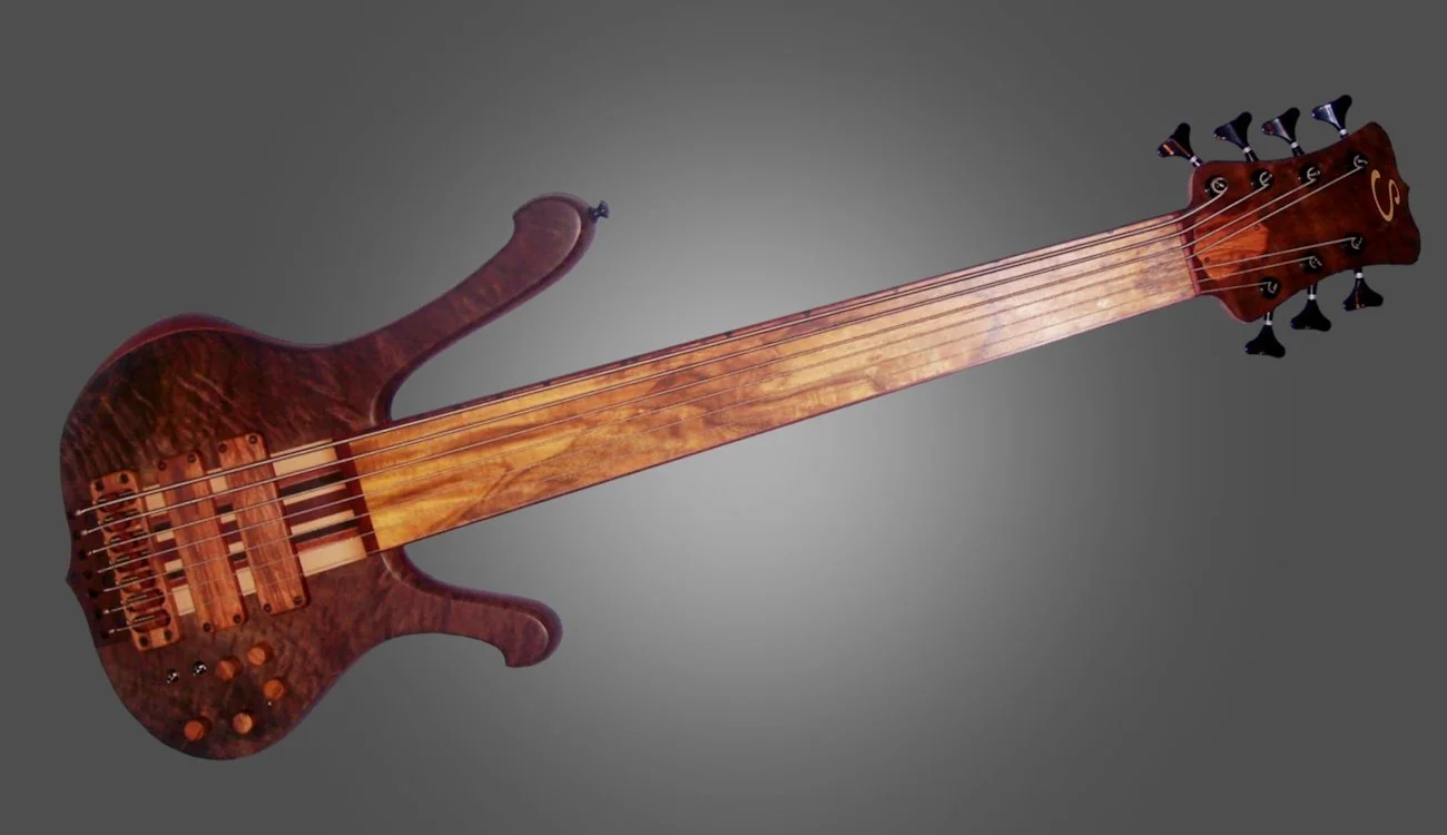 Wooden electric bass guitar with a natural finish and nine tuning pegs on the headstock, against a plain gray background.
