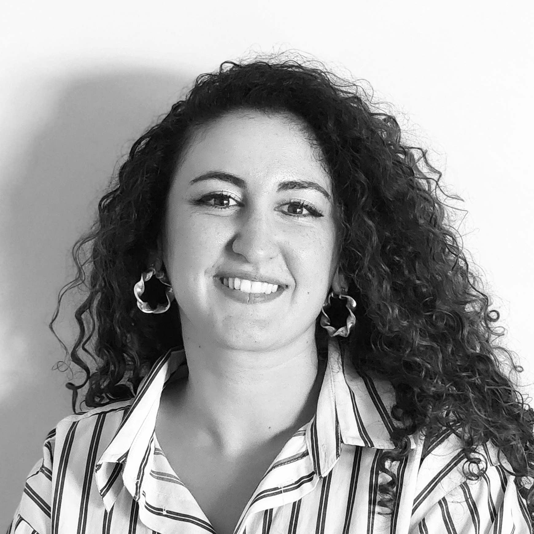 Black and white portrait of a smiling woman with curly hair, wearing hoop earrings and a striped shirt.