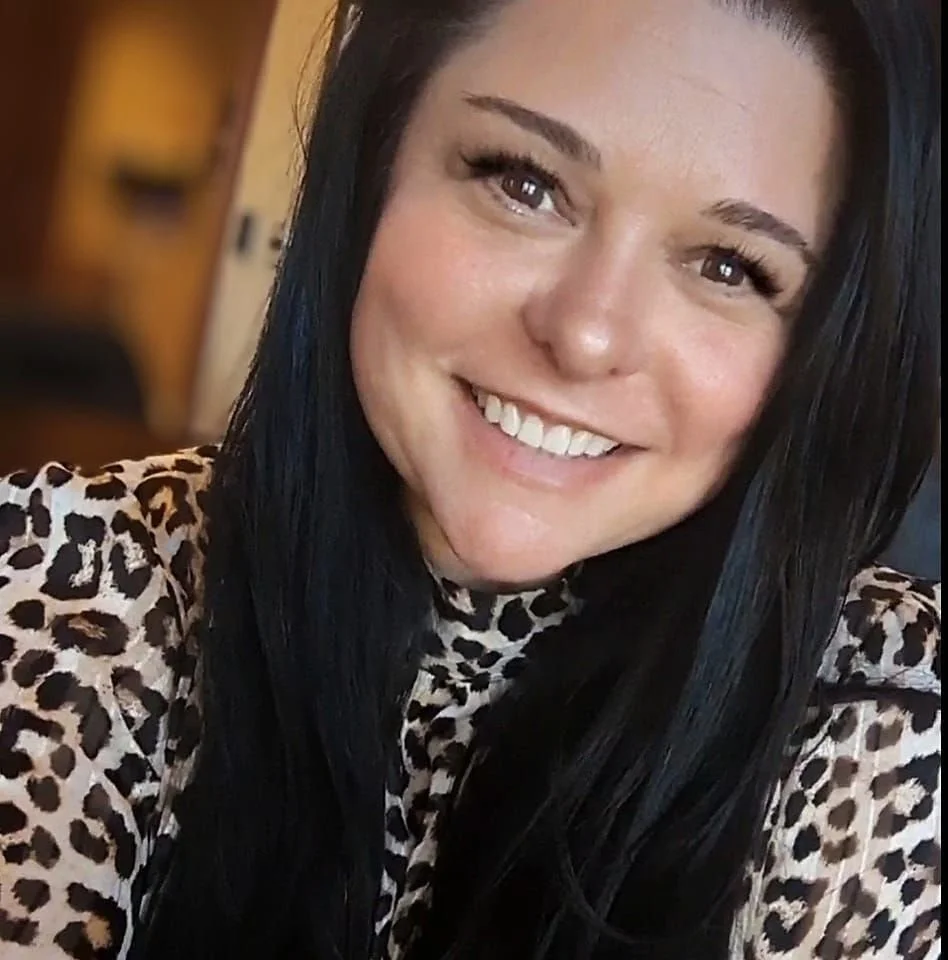 A woman with long black hair smiling, wearing a leopard print top.