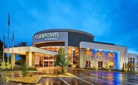 Hotel entrance of Four Points by Sheraton at dusk, with modern architecture, blue accent lighting, and a clear evening sky.