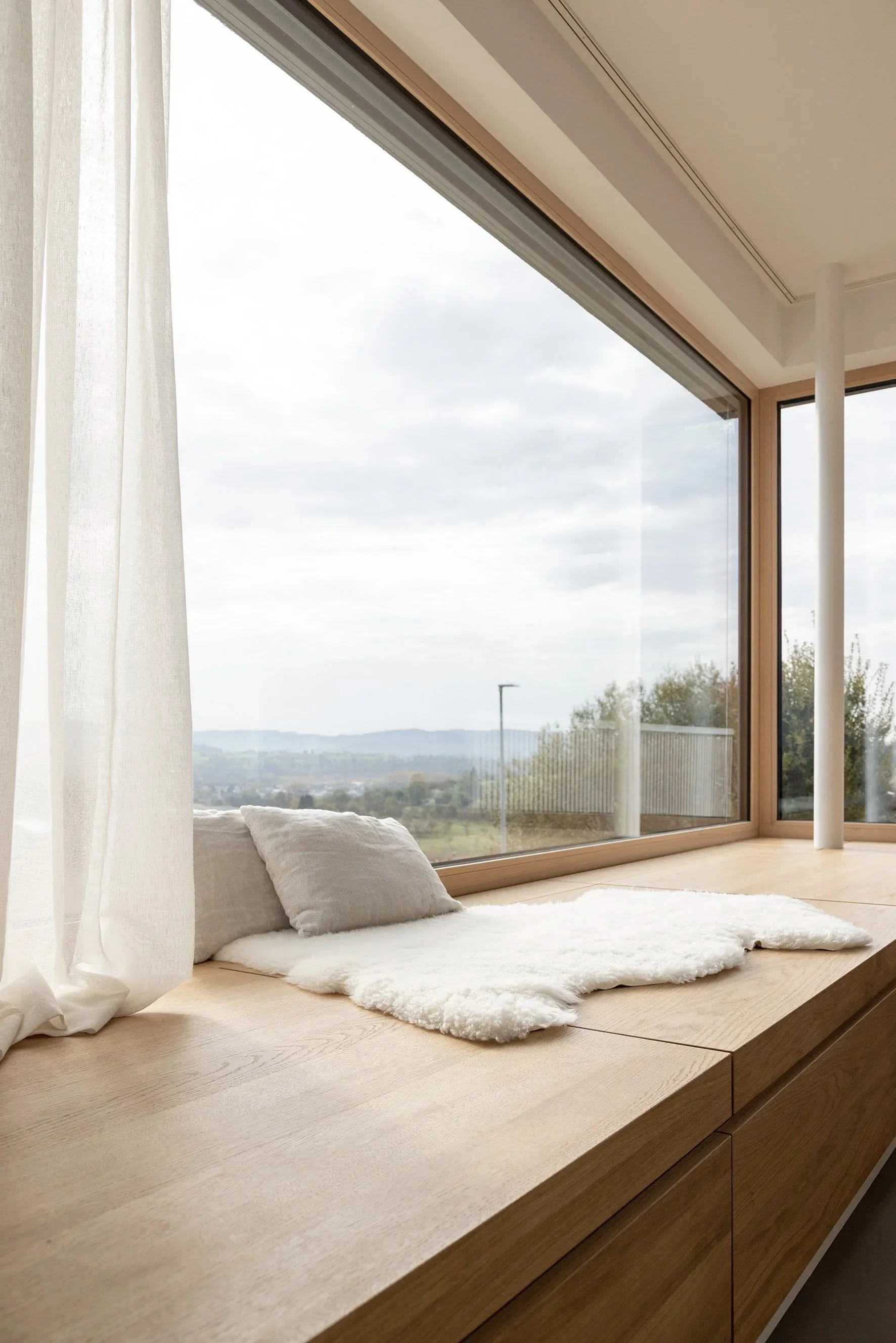 Sitzfenster mit Sitzmöbel aus geöltem Eichenholz, bestechende Aussicht, natürliche Materialien.