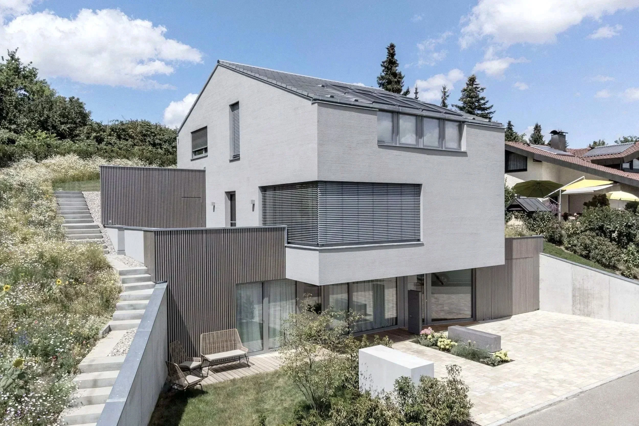 Modernes graues Haus mit einer Fassade mit Besenstrichputz, minimalistische Architektur. Hangbauweise. Haus auf der Blumenwiese.