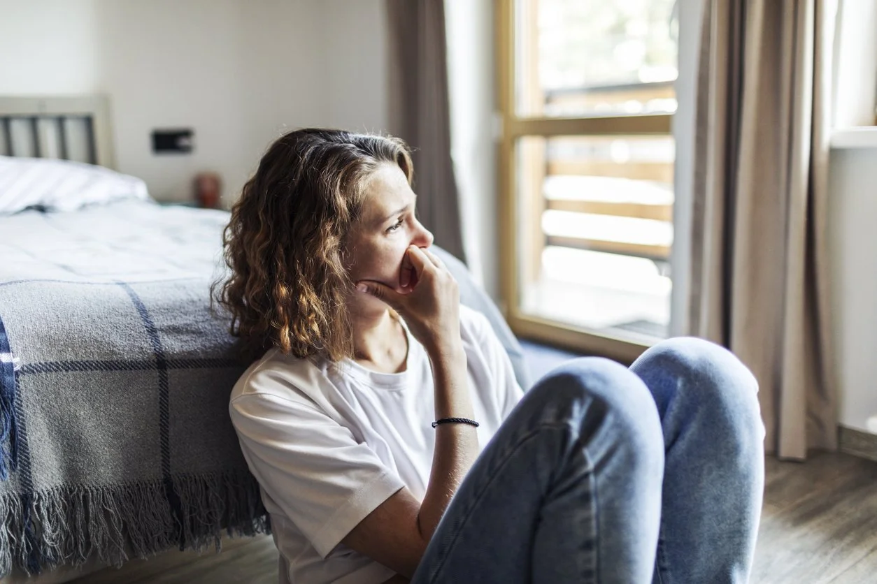 woman with blonde curly hair sitting on the floor looking sad